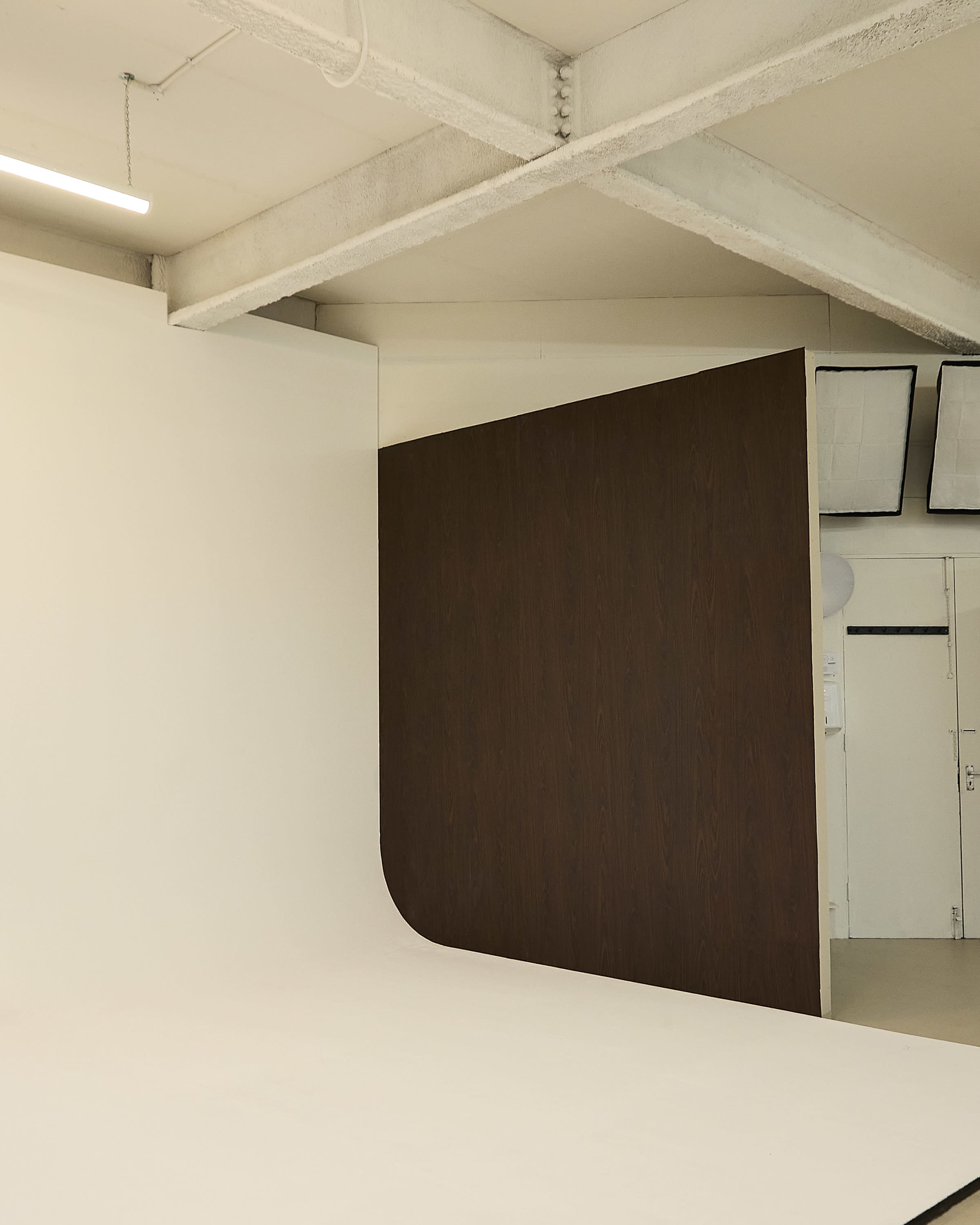 The image shows an empty photography studio with a seamless white backdrop and a curved wooden wall.