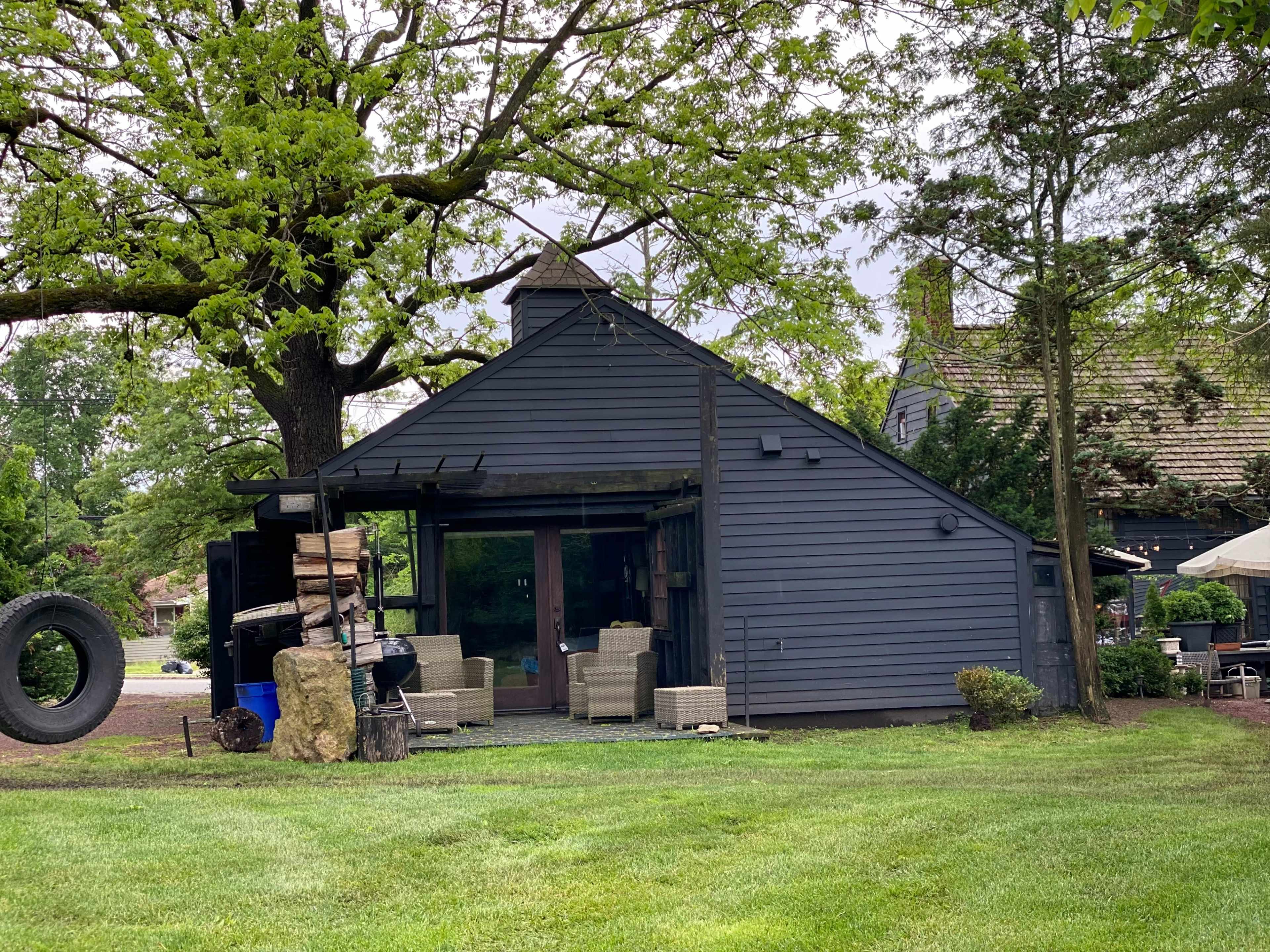 A modern, sloped-roof house with dark gray siding is surrounded by green grass and trees.