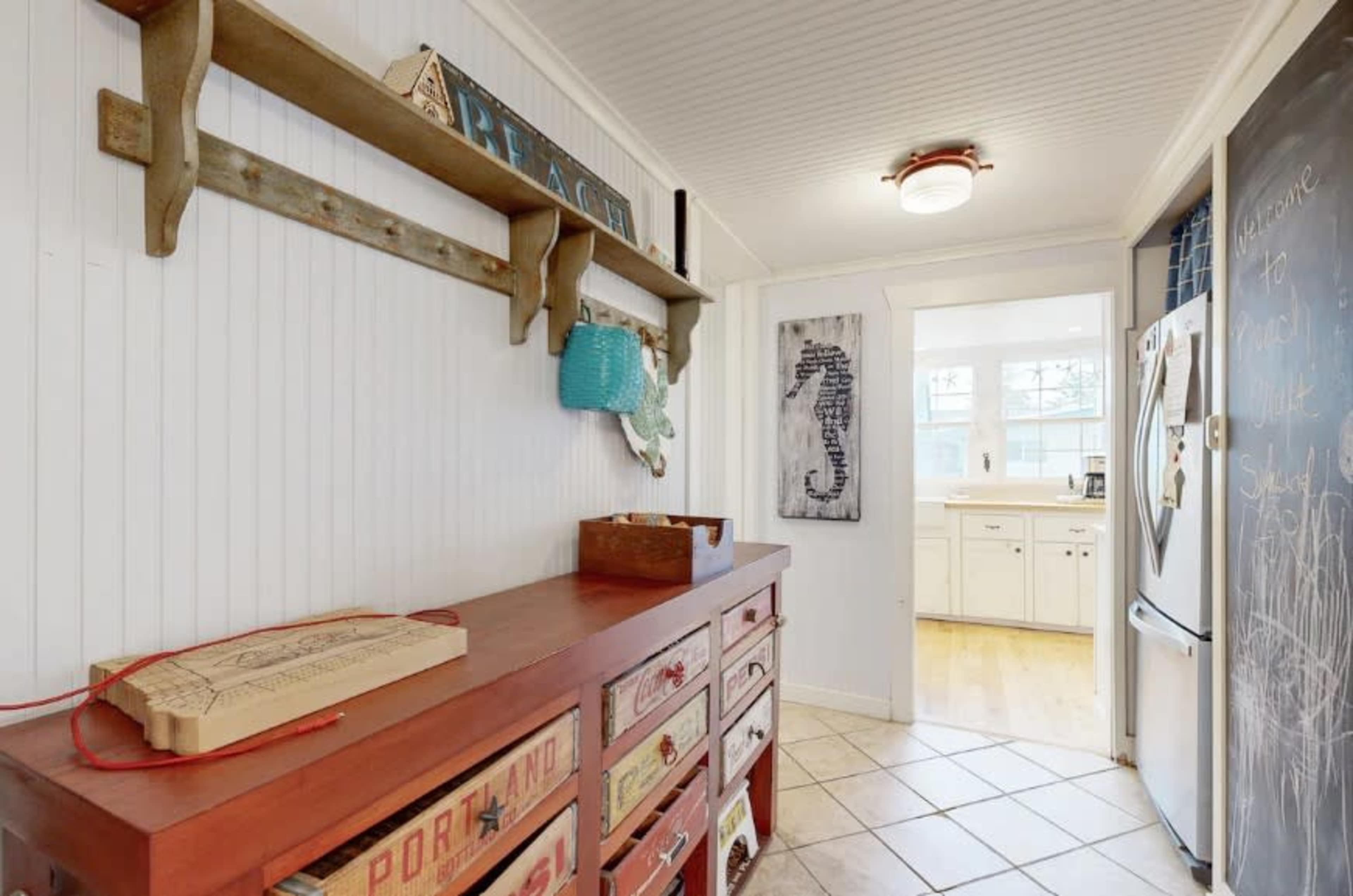 A hallway features a wooden shelf above a red dresser, leading to a bright kitchen area visible in the background.
