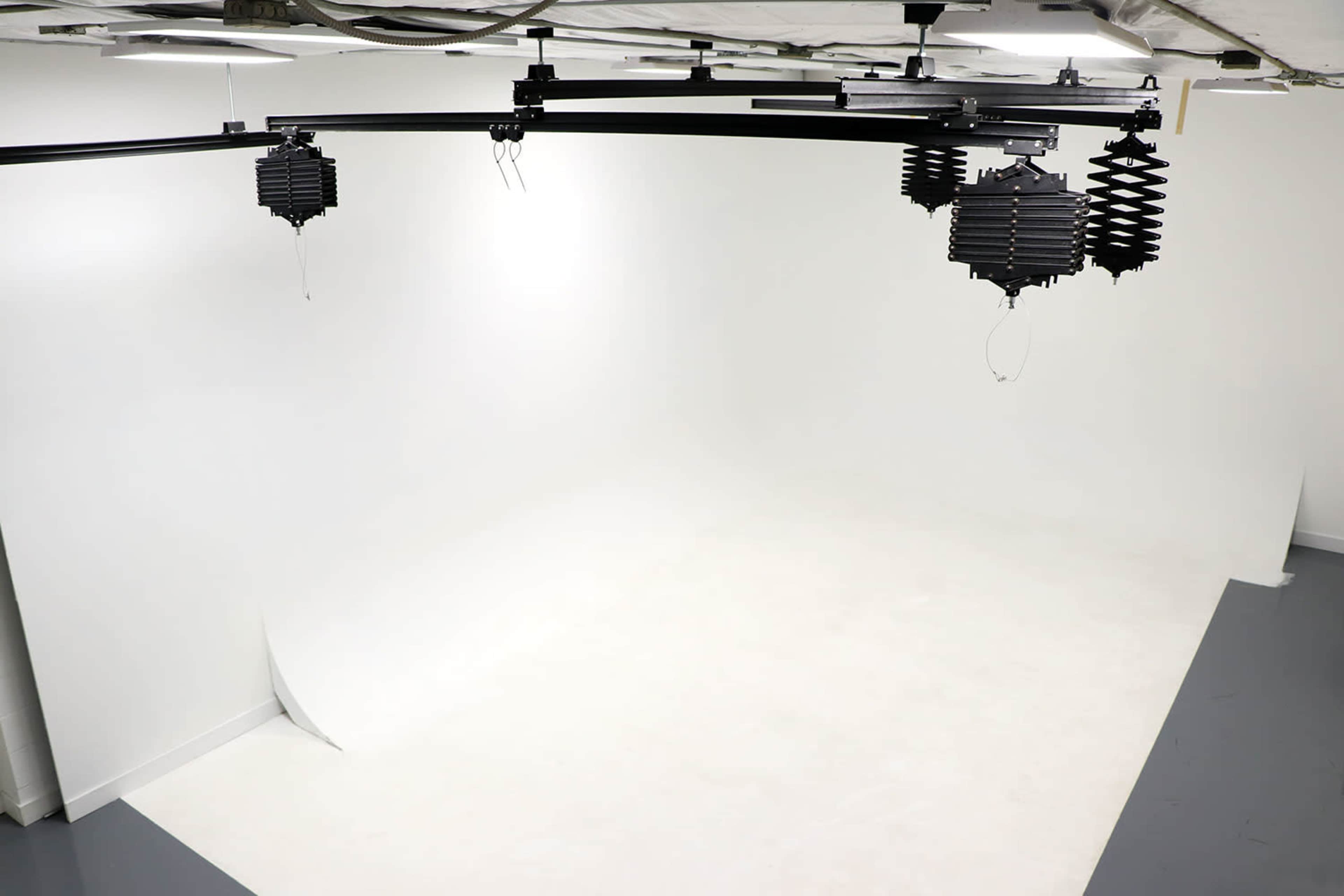 A well-lit photography studio with a seamless white backdrop and overhead lighting fixtures.