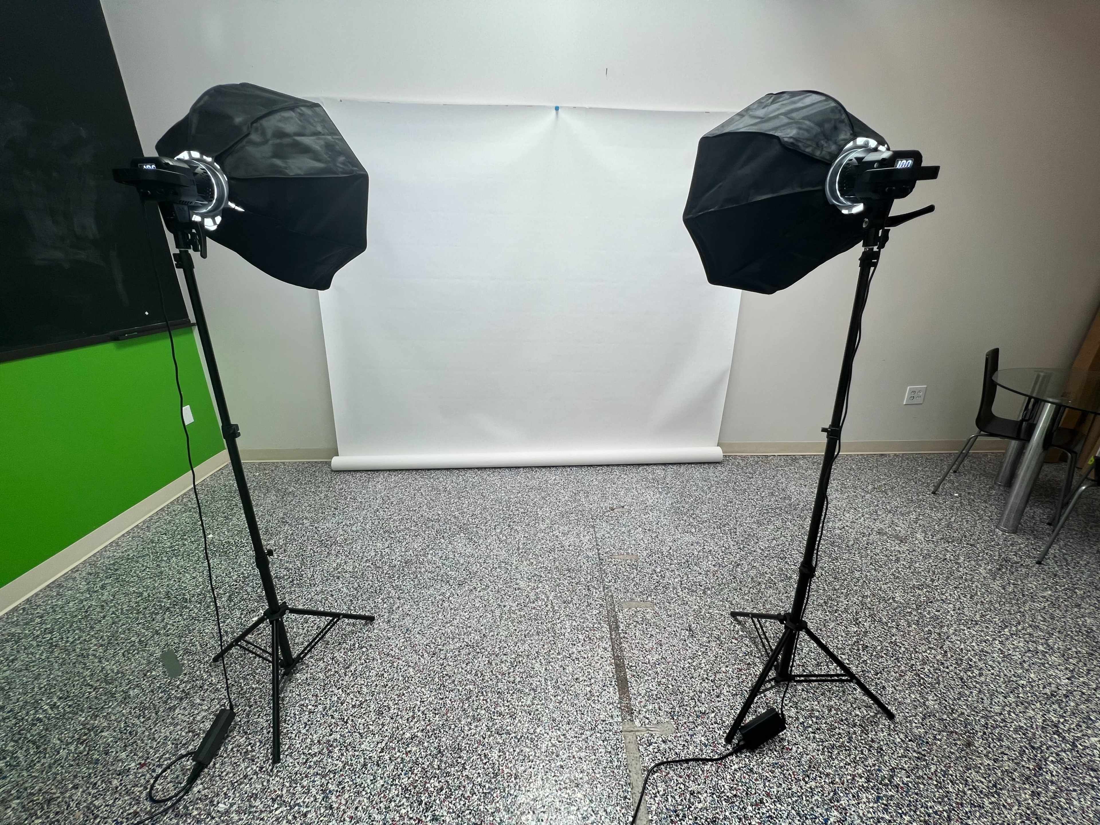 Two softbox lights are set up on tripods facing a white backdrop in a room with a green wall.