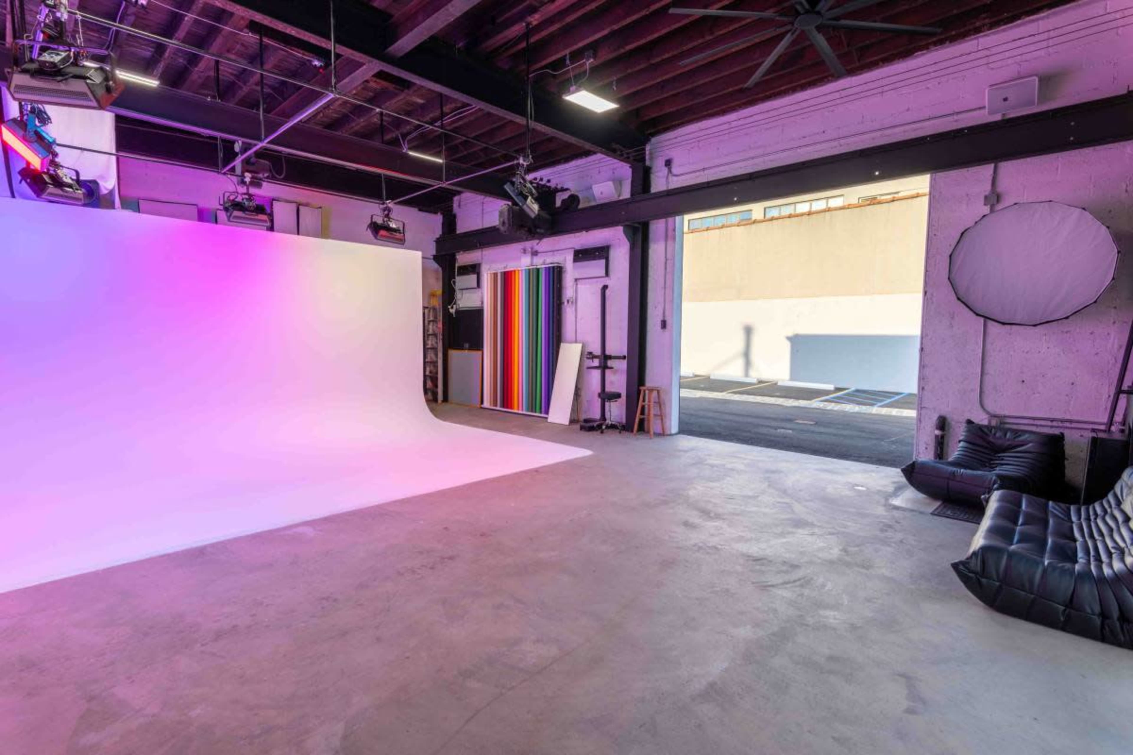 The image shows a spacious studio with a gradient background setup, colorful backdrops, and a seating area visible in the corner.