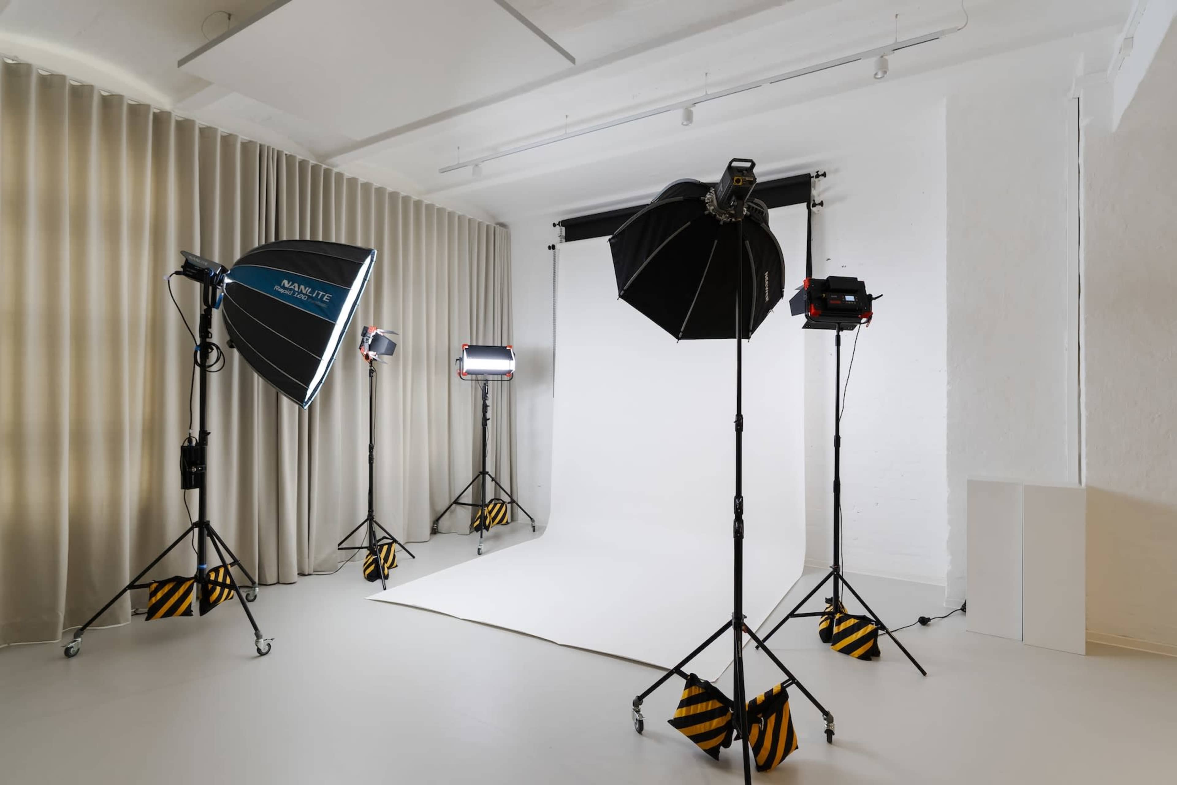 The image shows a photography studio equipped with various lighting setups and a blank backdrop.