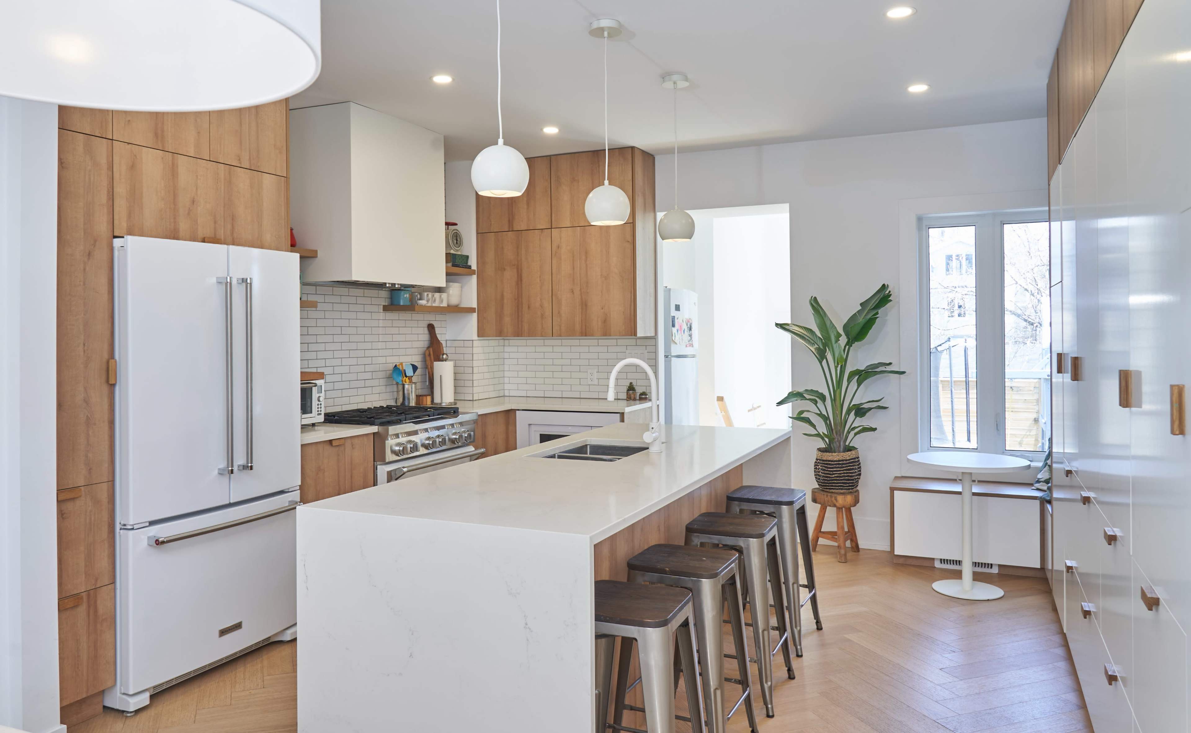 A modern kitchen featuring wooden cabinets, a large white island with seating, and stainless steel appliances.
