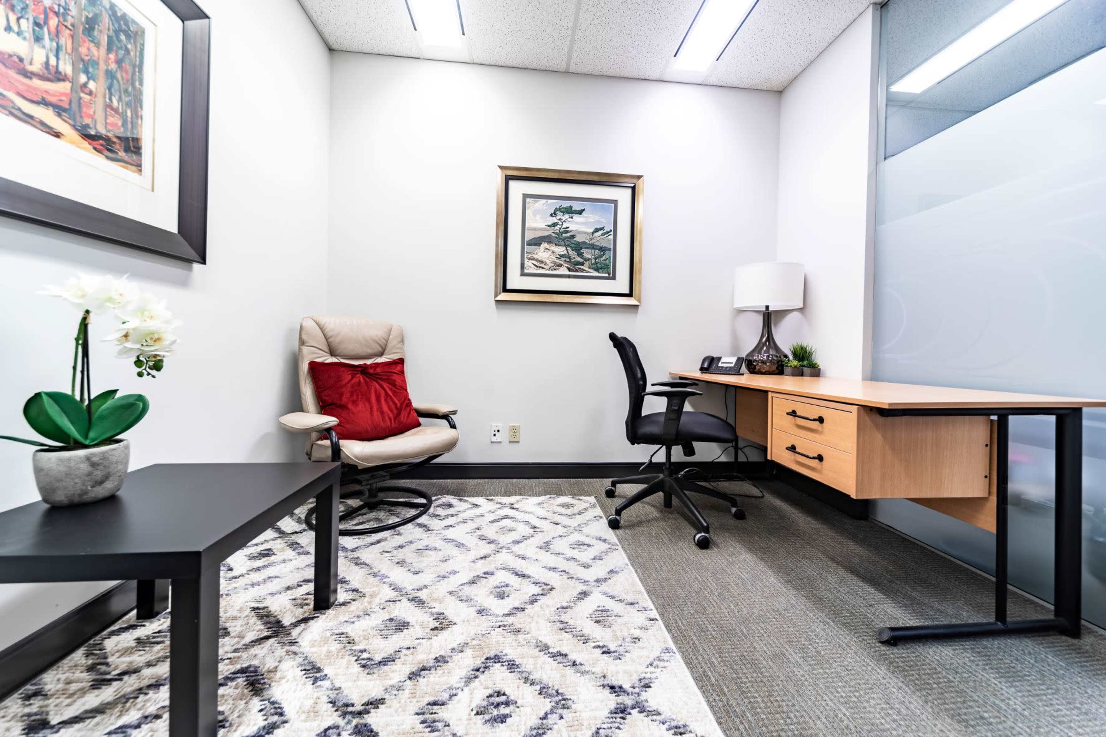 A minimalist office space featuring a desk, a chair, a recliner, a small table, and a framed picture on the wall.