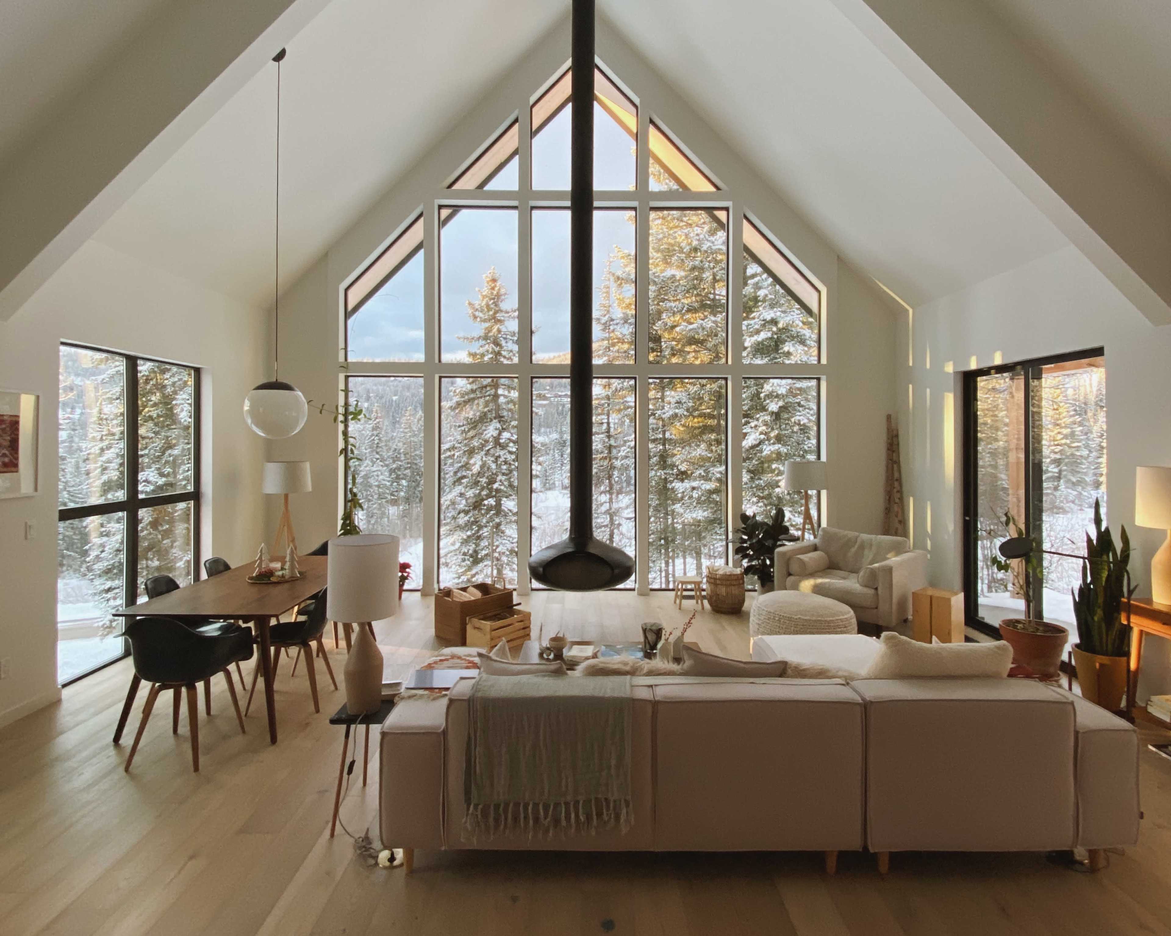 The living room features large windows overlooking a snowy forest, with modern furniture arranged around a central fireplace.