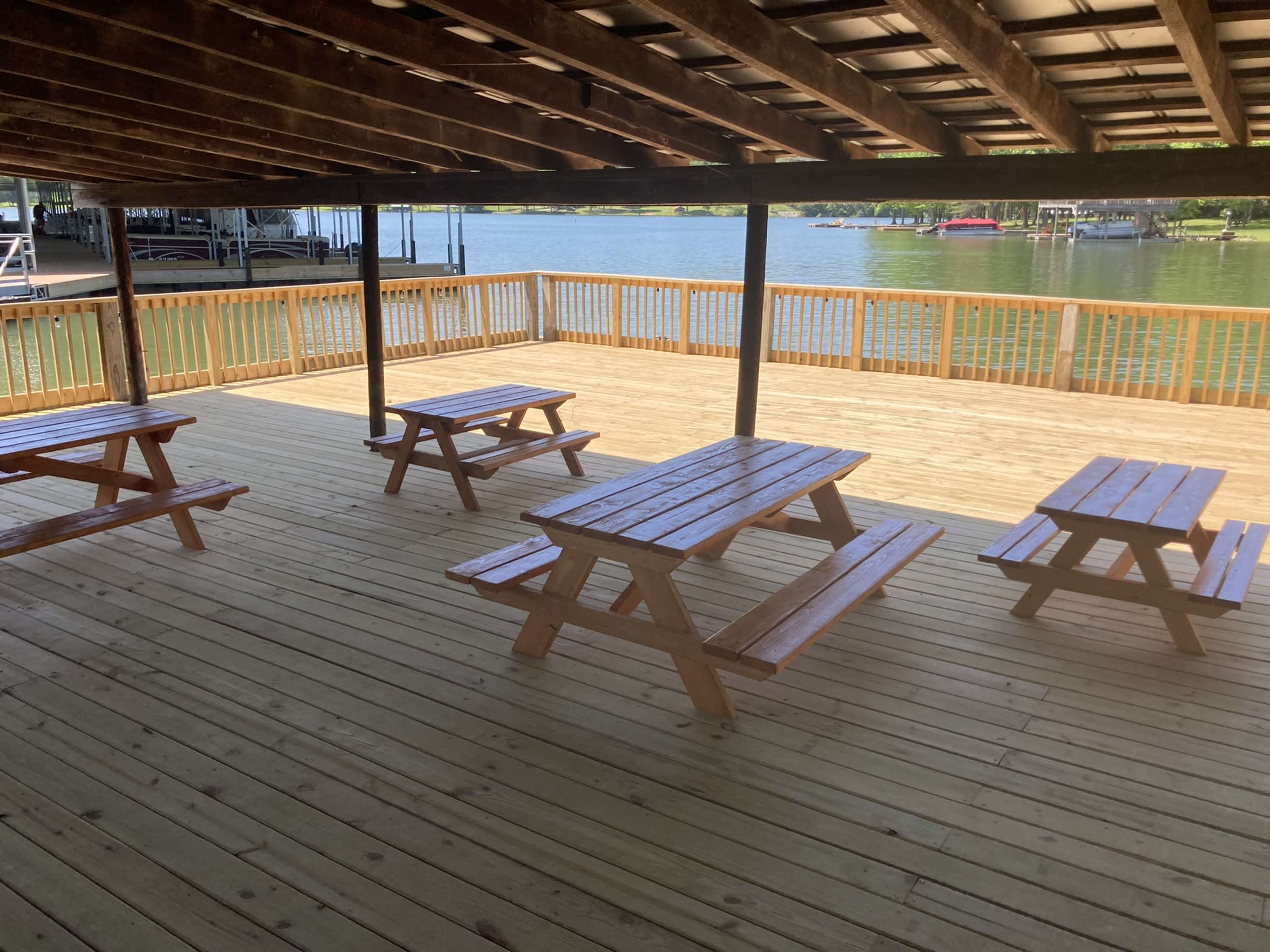 A wooden deck with several picnic tables overlooks a calm body of water.
