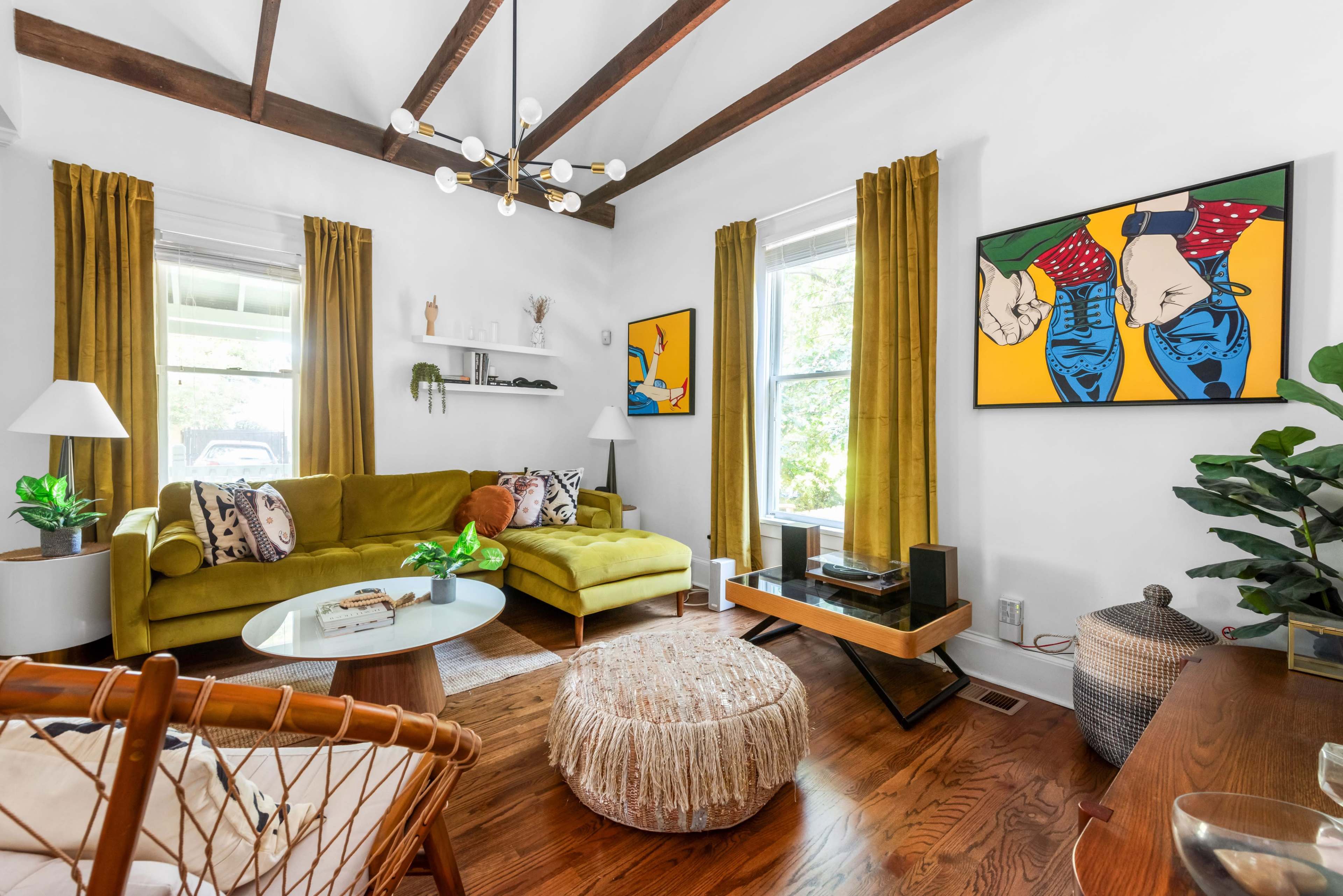 The image features a bright living room with a green sectional sofa, wooden beams, and two colorful artworks on the walls.