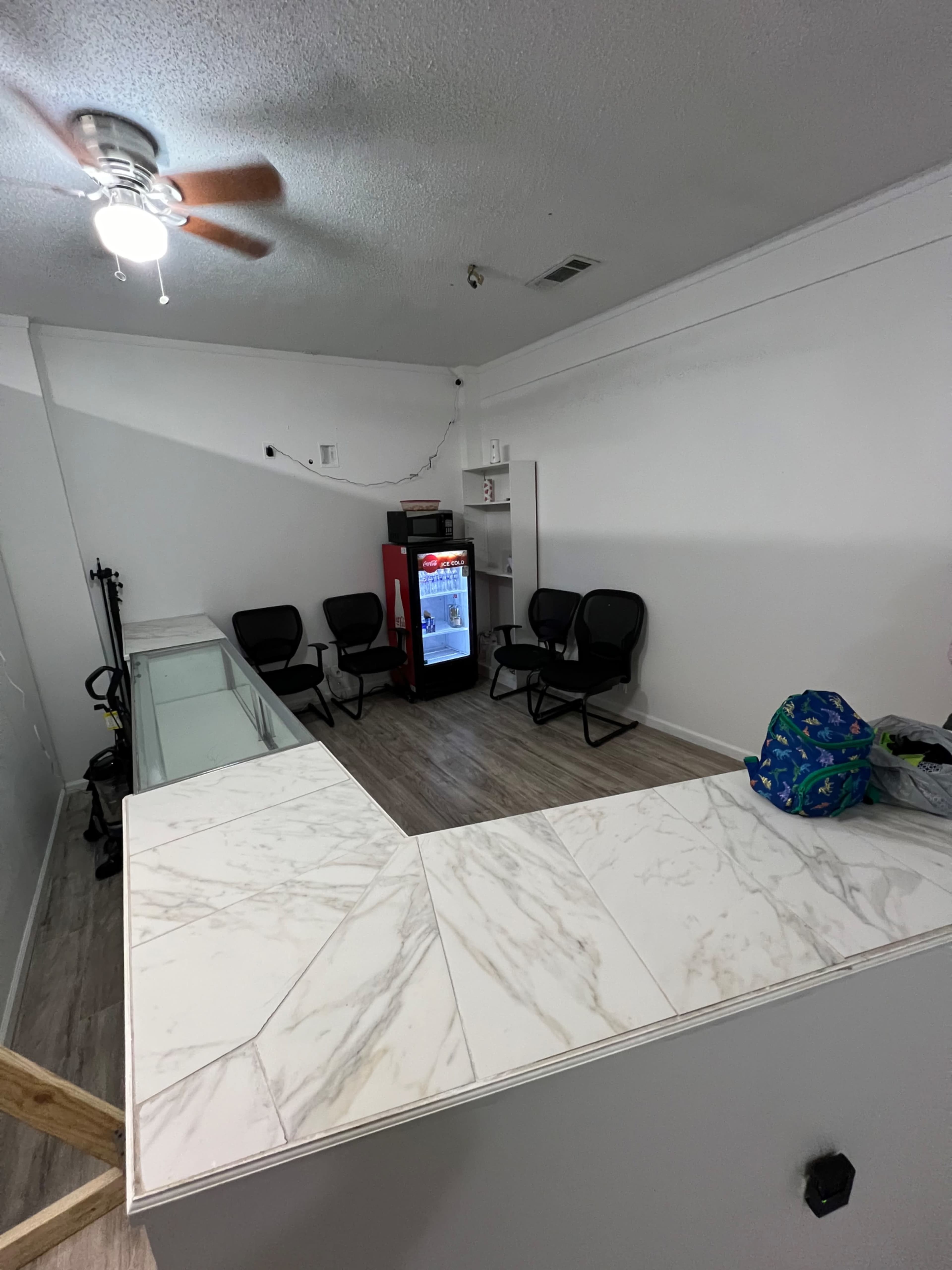 A small waiting area with four black chairs, a refrigerator, and a countertop in a brightly lit room.