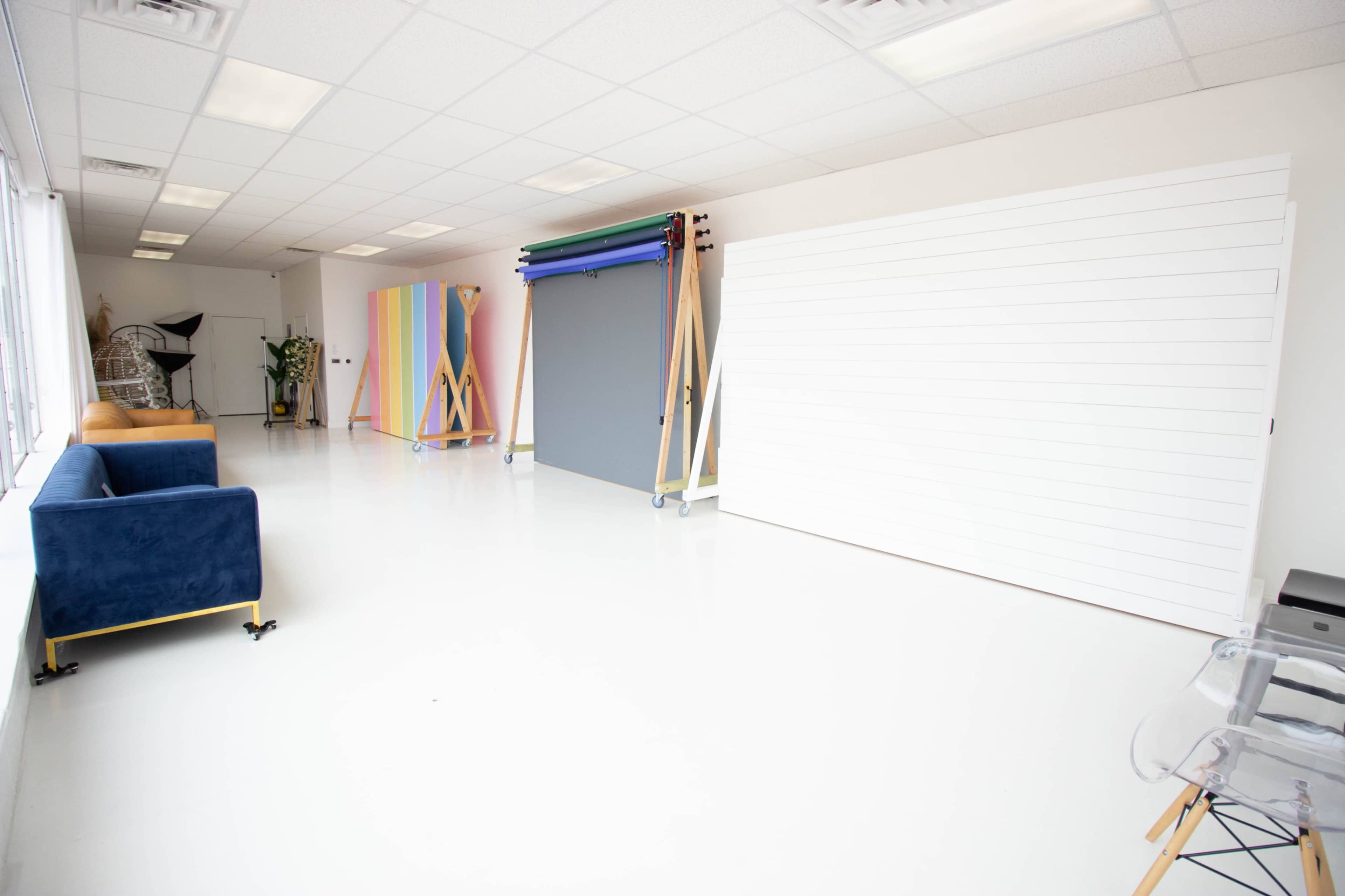 The image shows a bright, spacious studio with white floors, a blue couch, and several backdrops on display.