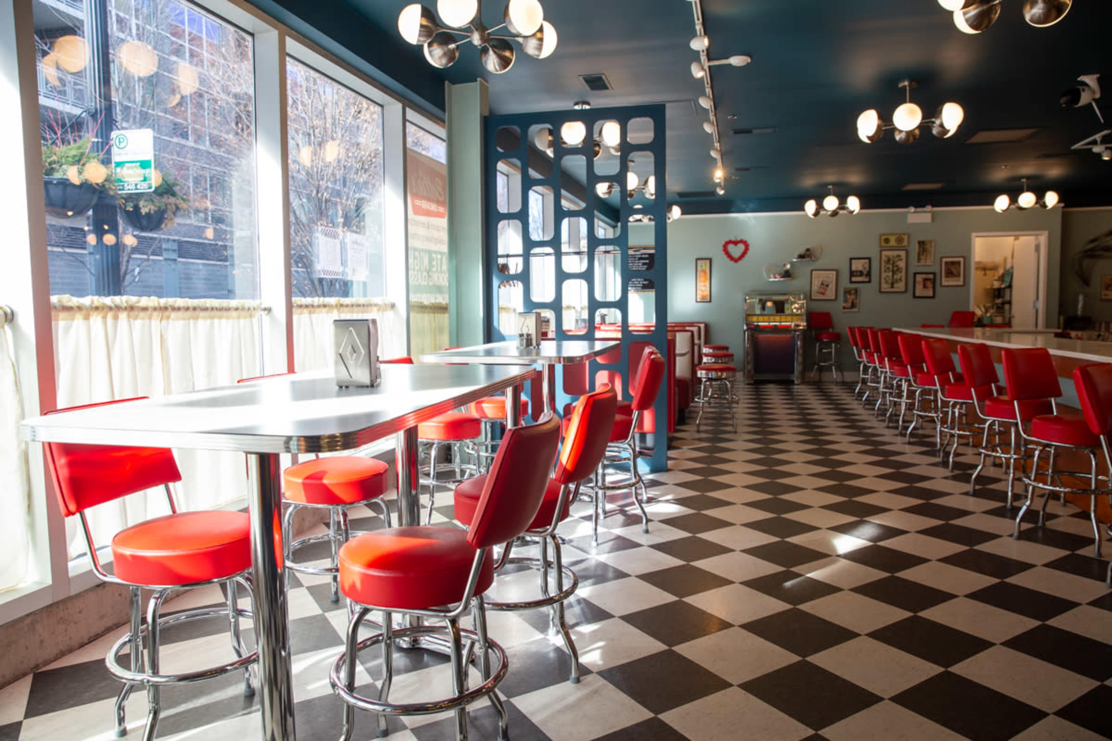 A retro-style diner with red bar stools and a checkered floor, illuminated by round ceiling lights.