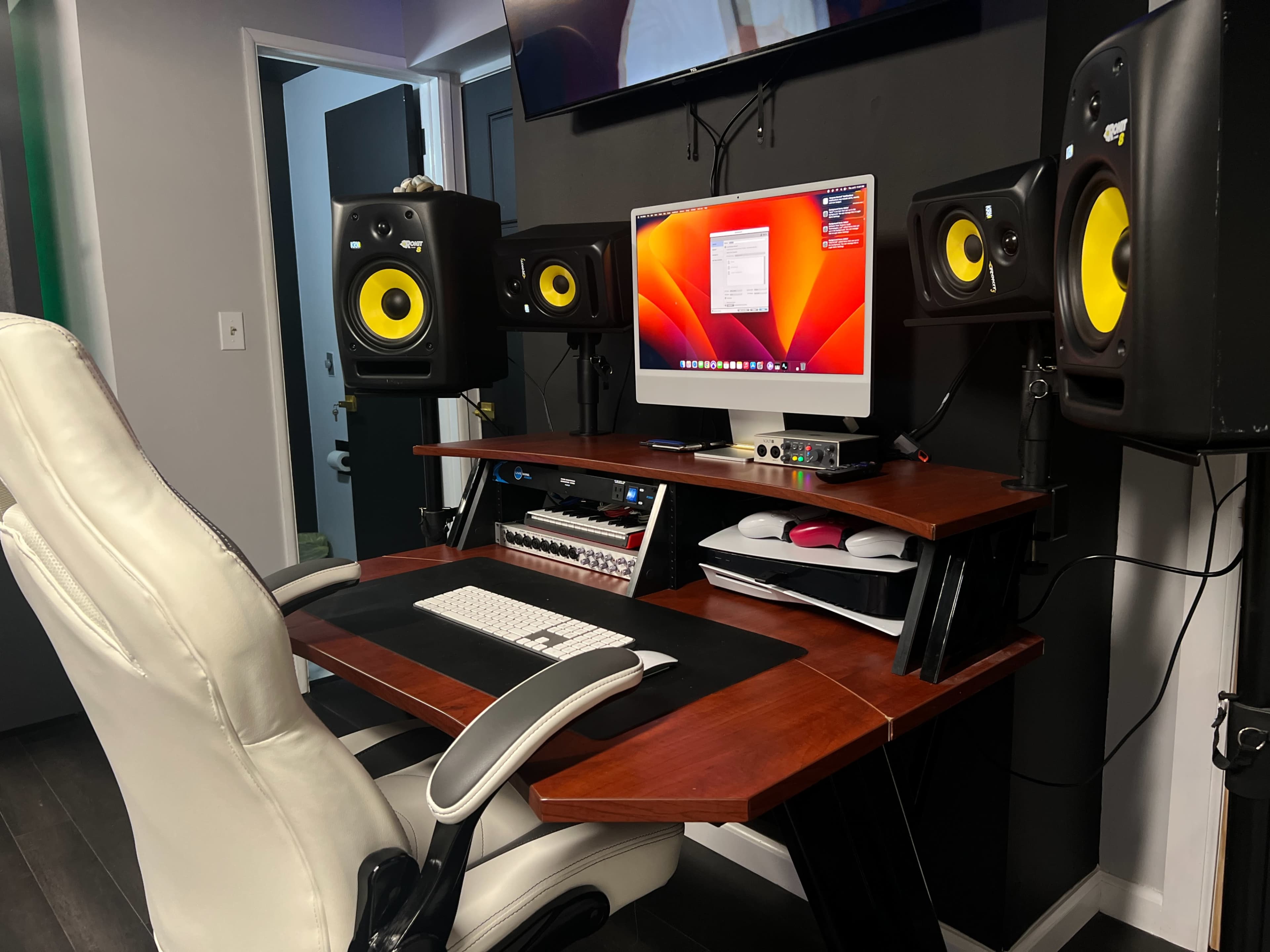 A workspace featuring a wooden desk with a computer monitor, audio speakers on either side, and a keyboard, all arranged in a modern studio setup.
