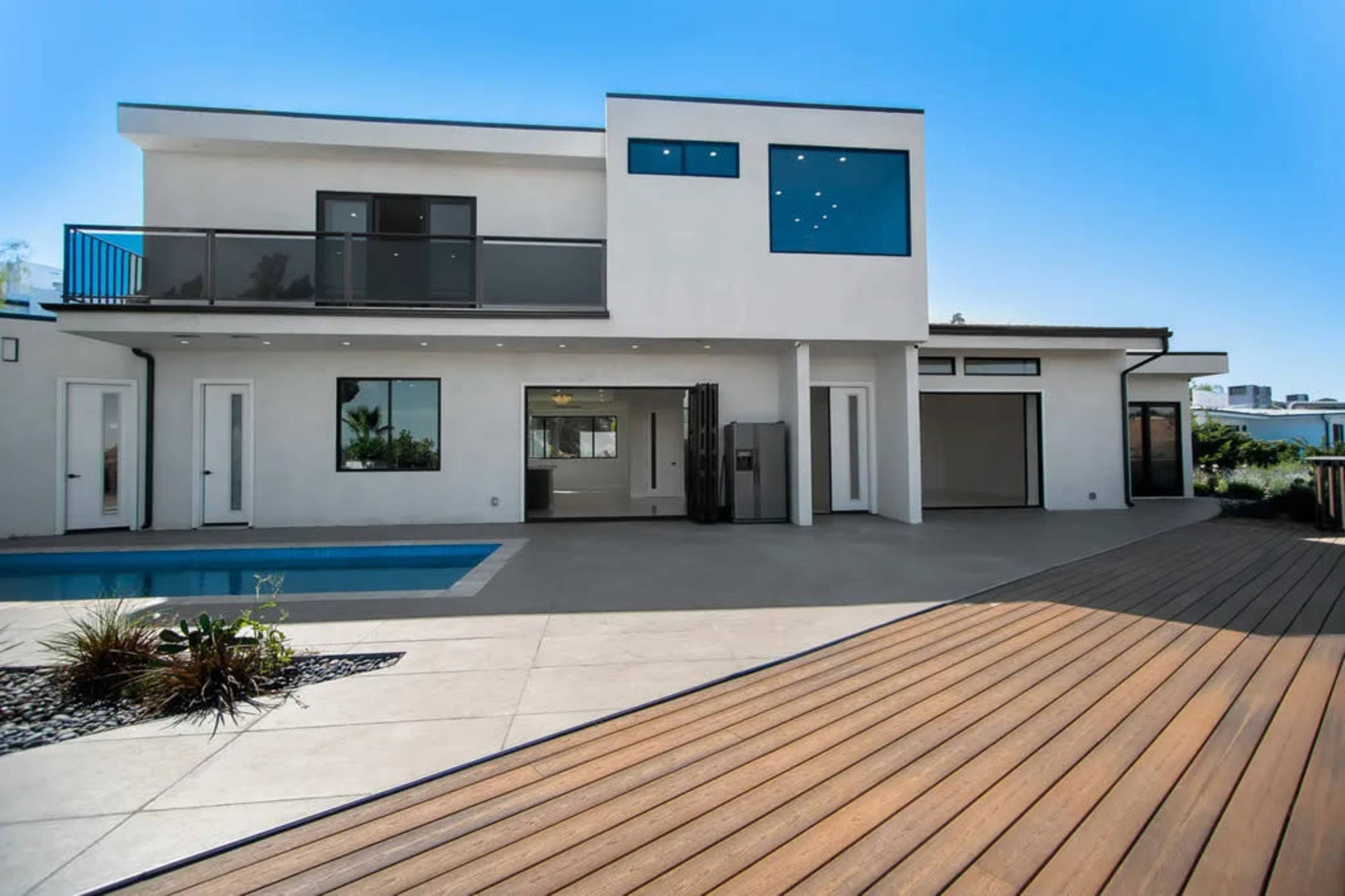 A modern two-story house features large windows, a balcony, and a swimming pool in the backyard.