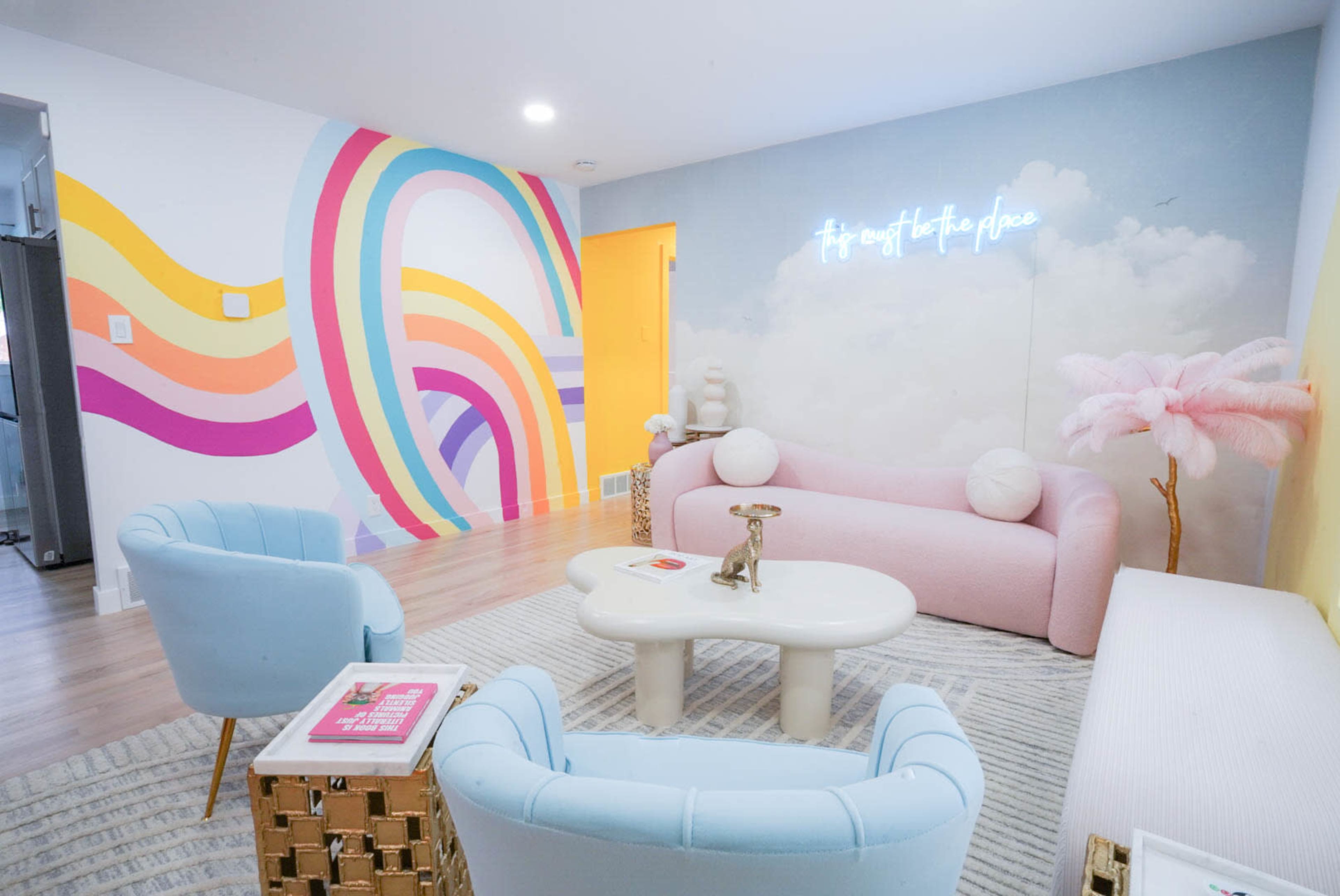 A brightly colored lounge area with pastel furniture, a rainbow mural on the wall, and a neon sign that reads "It's easy to take place."
