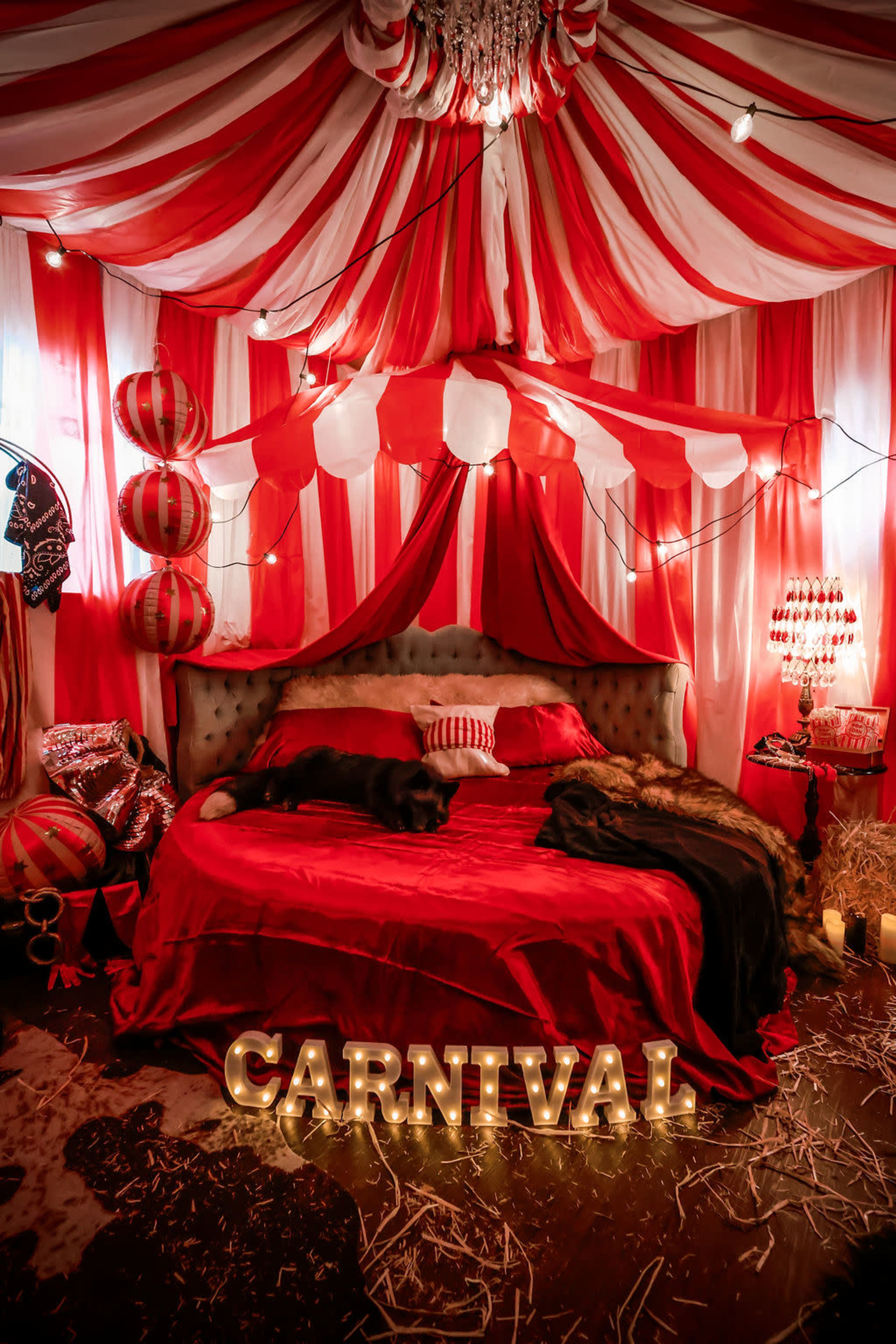 The scene features a vibrant, carnival-themed bedroom adorned with red and white striped drapery, string lights, and decorative elements like lanterns and a plush bed.