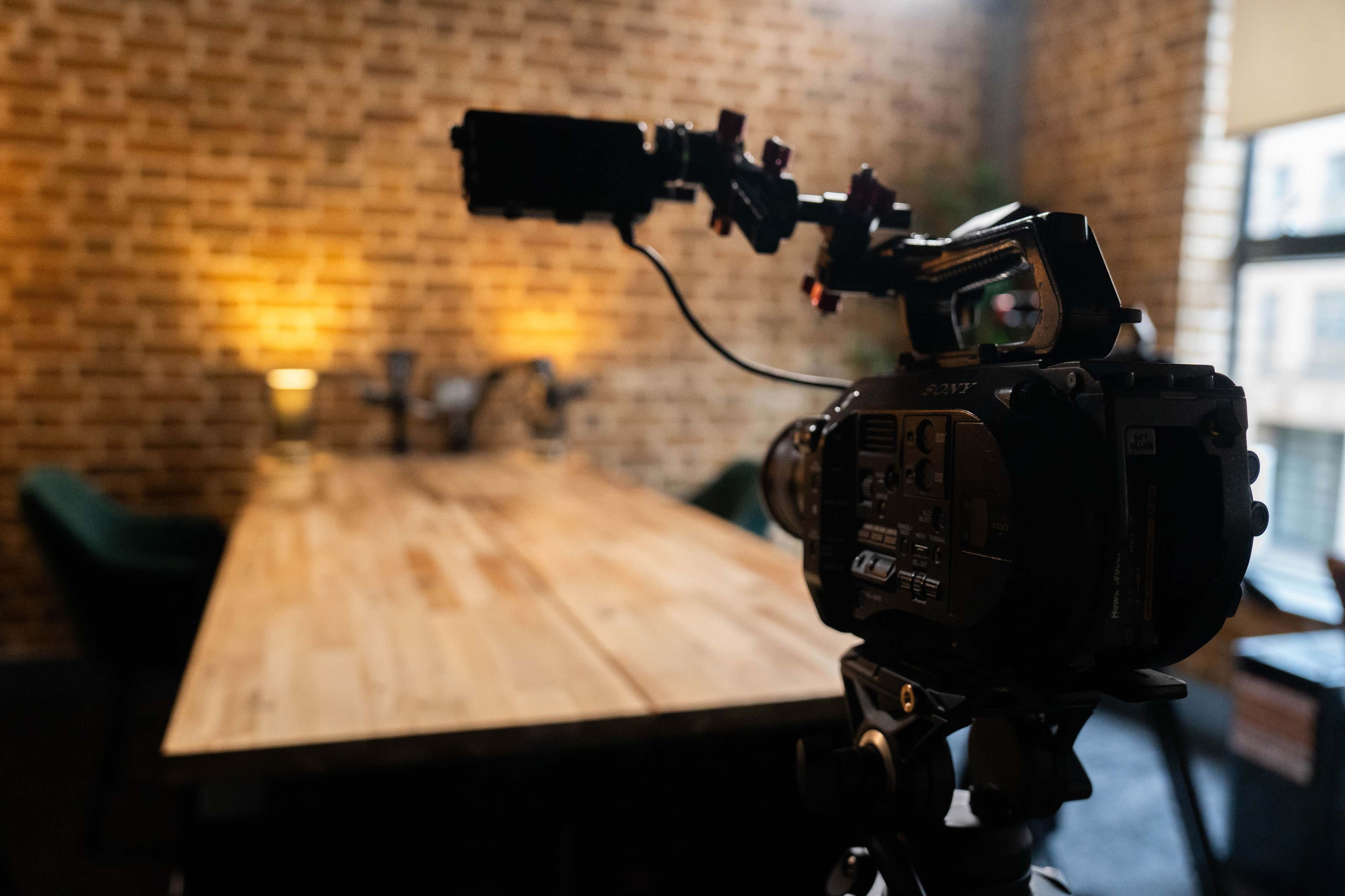 A camera is positioned in front of a wooden table in a room with a brick wall and soft lighting.