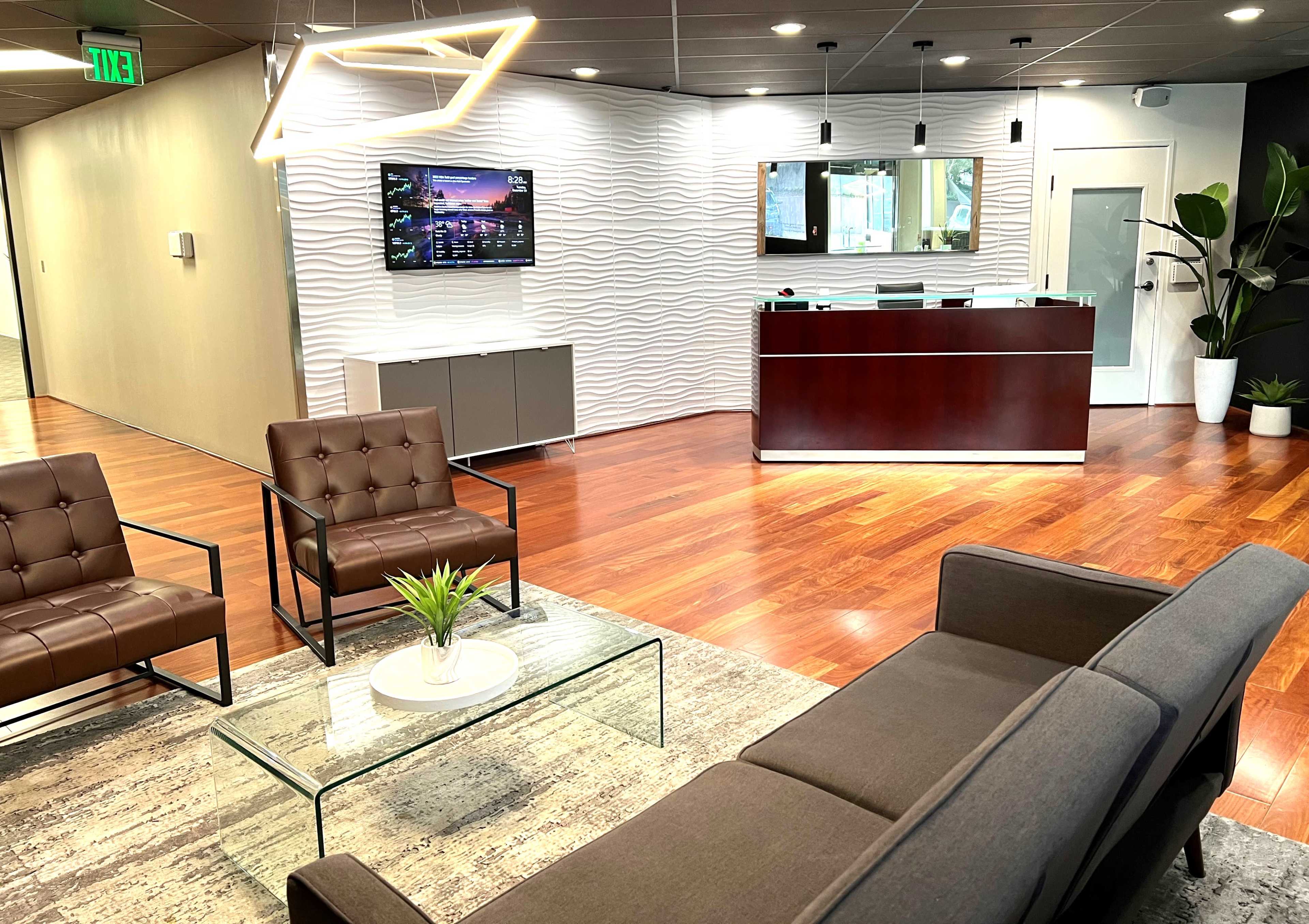 The reception area features modern furniture with a glass coffee table, a television on the wall, and a service desk behind a wavy panel.