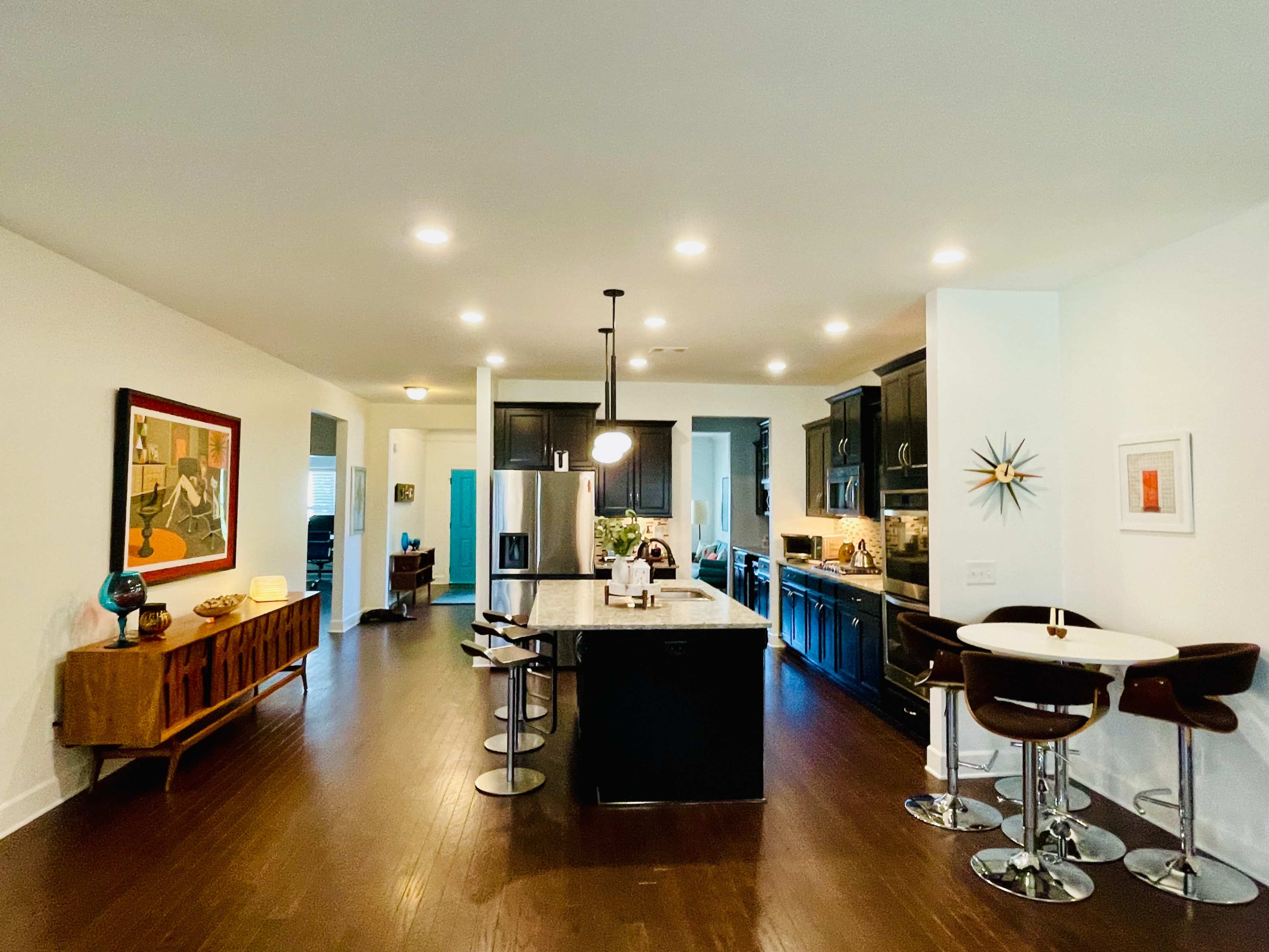 The image shows a modern kitchen with dark cabinetry, a central island with bar stools, and an open layout leading to a dining area.