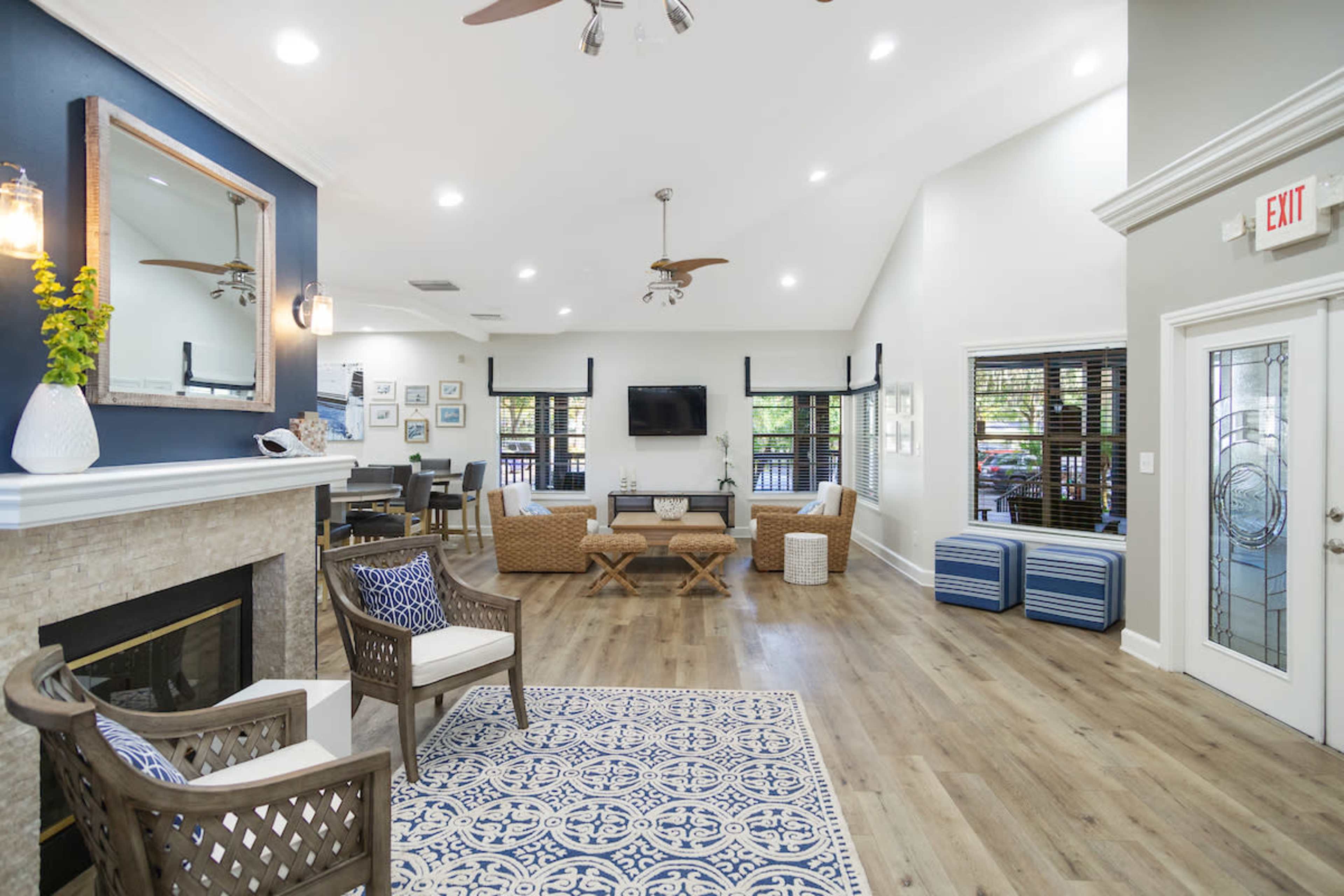 A well-lit common room with a fireplace, cozy seating, and a dining area, featuring large windows and wooden flooring.