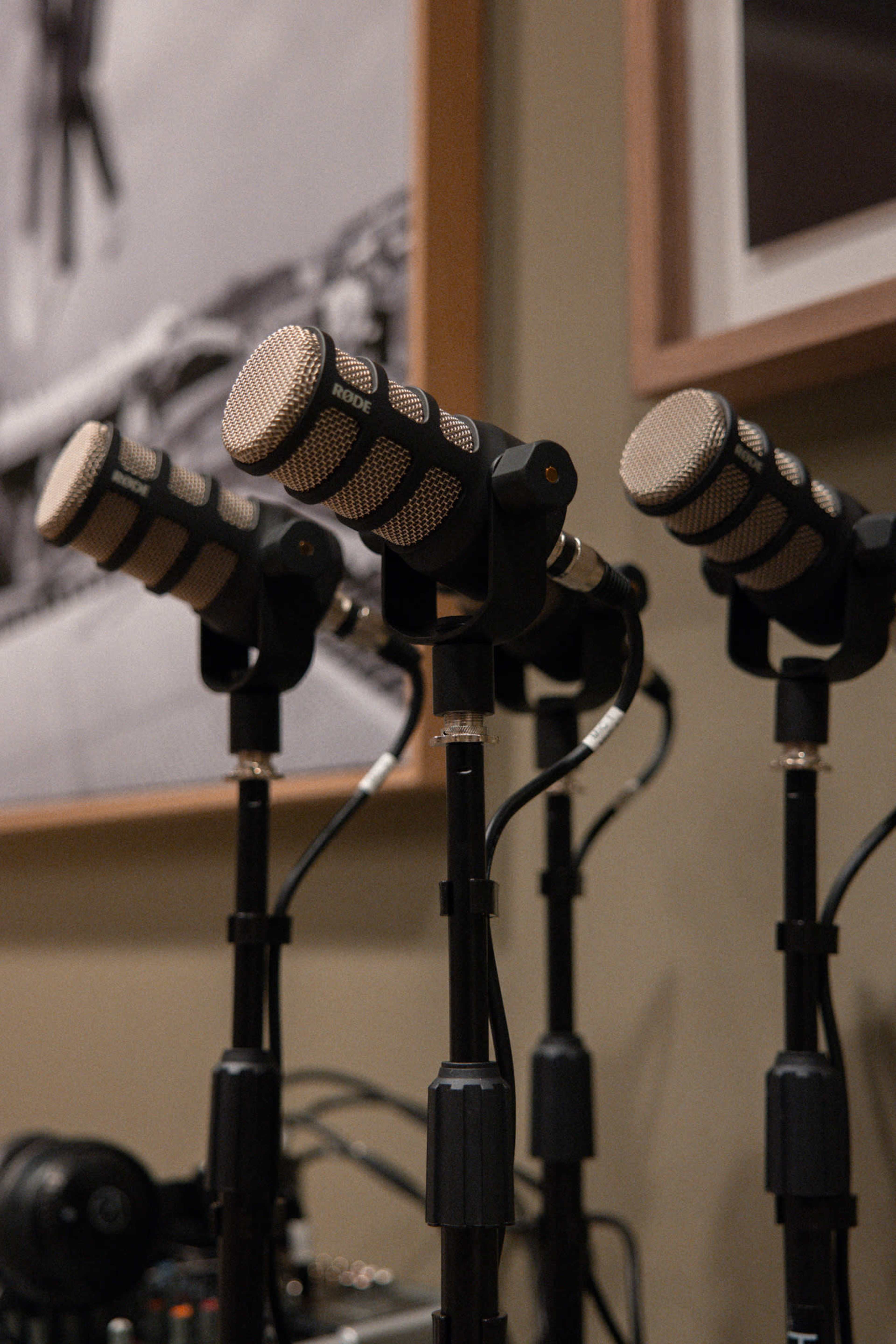 A row of microphones on stands is positioned against a wall with framed photographs.