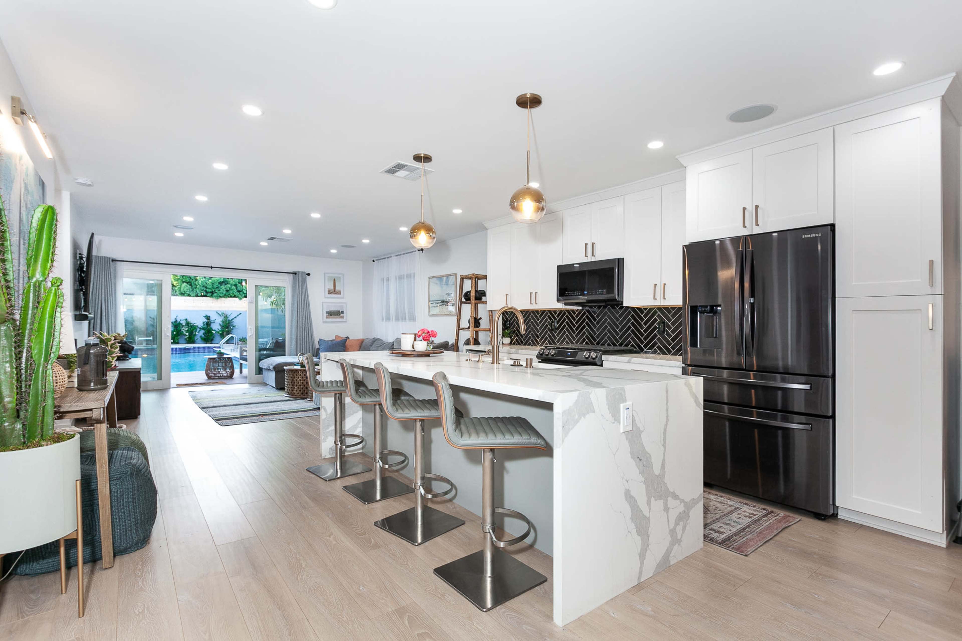 A modern kitchen with a large island and bar seating, connected to a living area with sliding glass doors leading to an outdoor space.