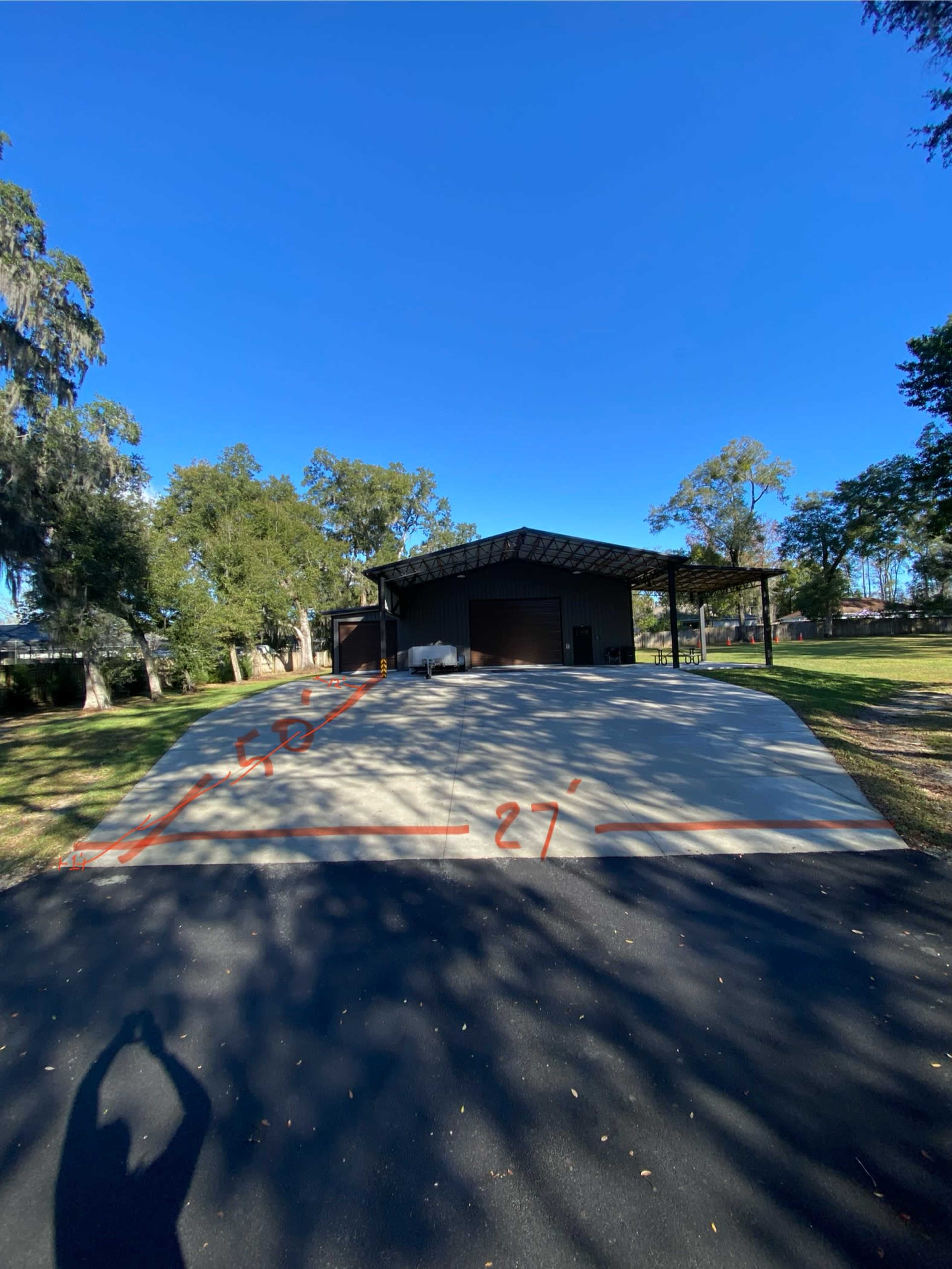 The image shows a large concrete pad in front of a metal building, marked with dimensions of 27 feet by 52 feet, surrounded by trees and grass.