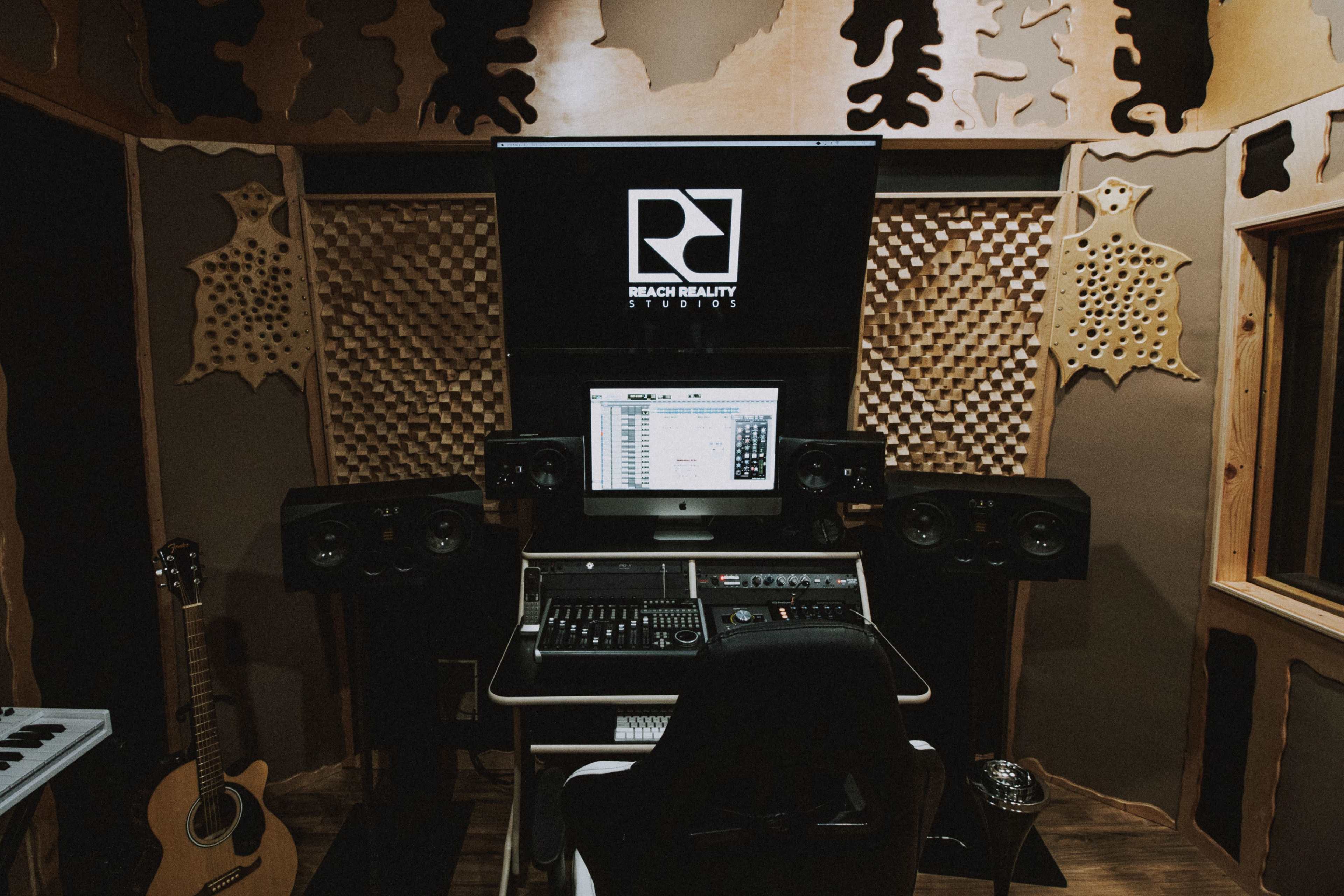 A music recording studio featuring a computer workstation with speakers, acoustic panels, and musical instruments.