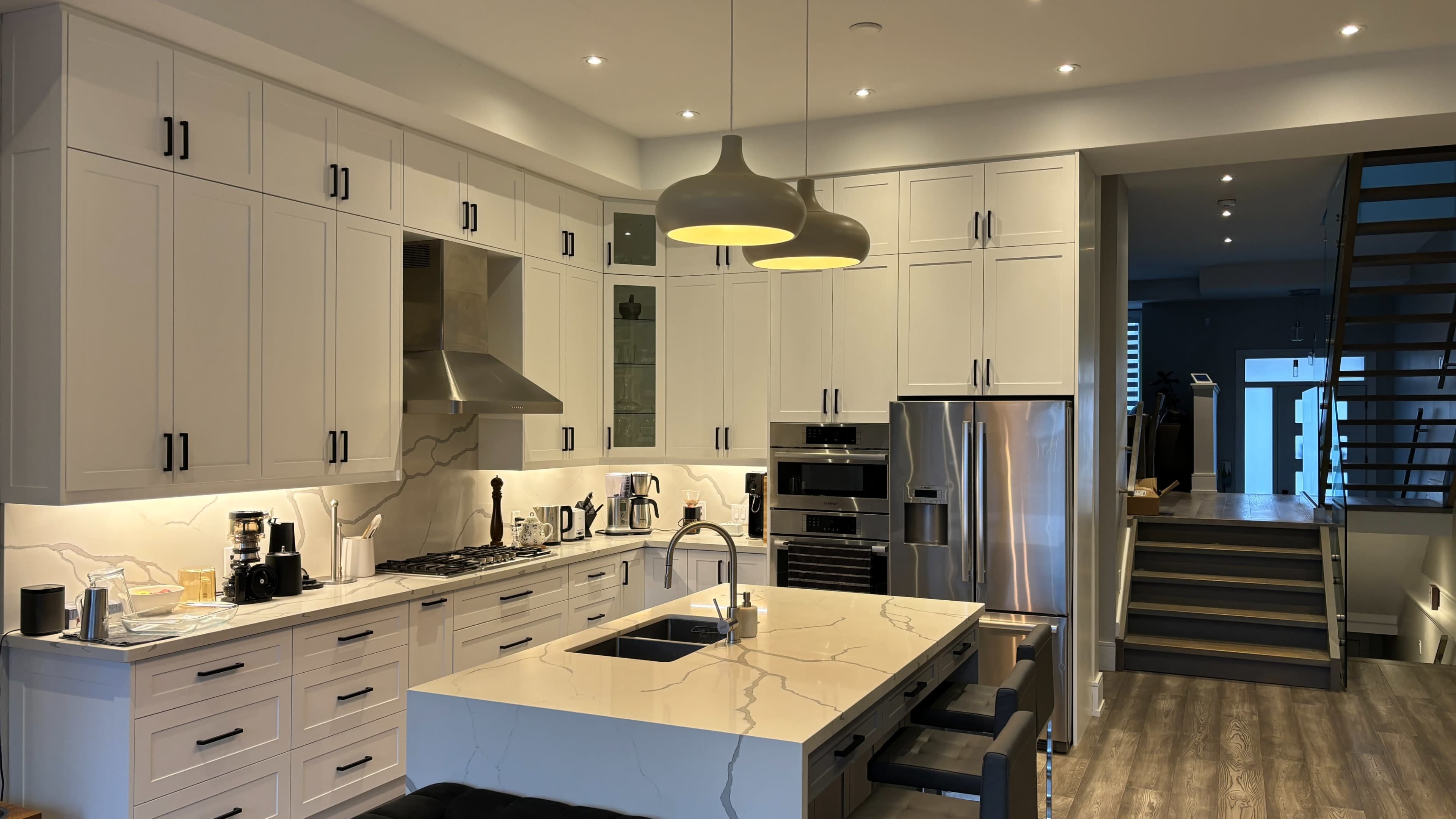 A modern kitchen featuring white cabinetry, a central island with a marble countertop, and two pendant lights above.