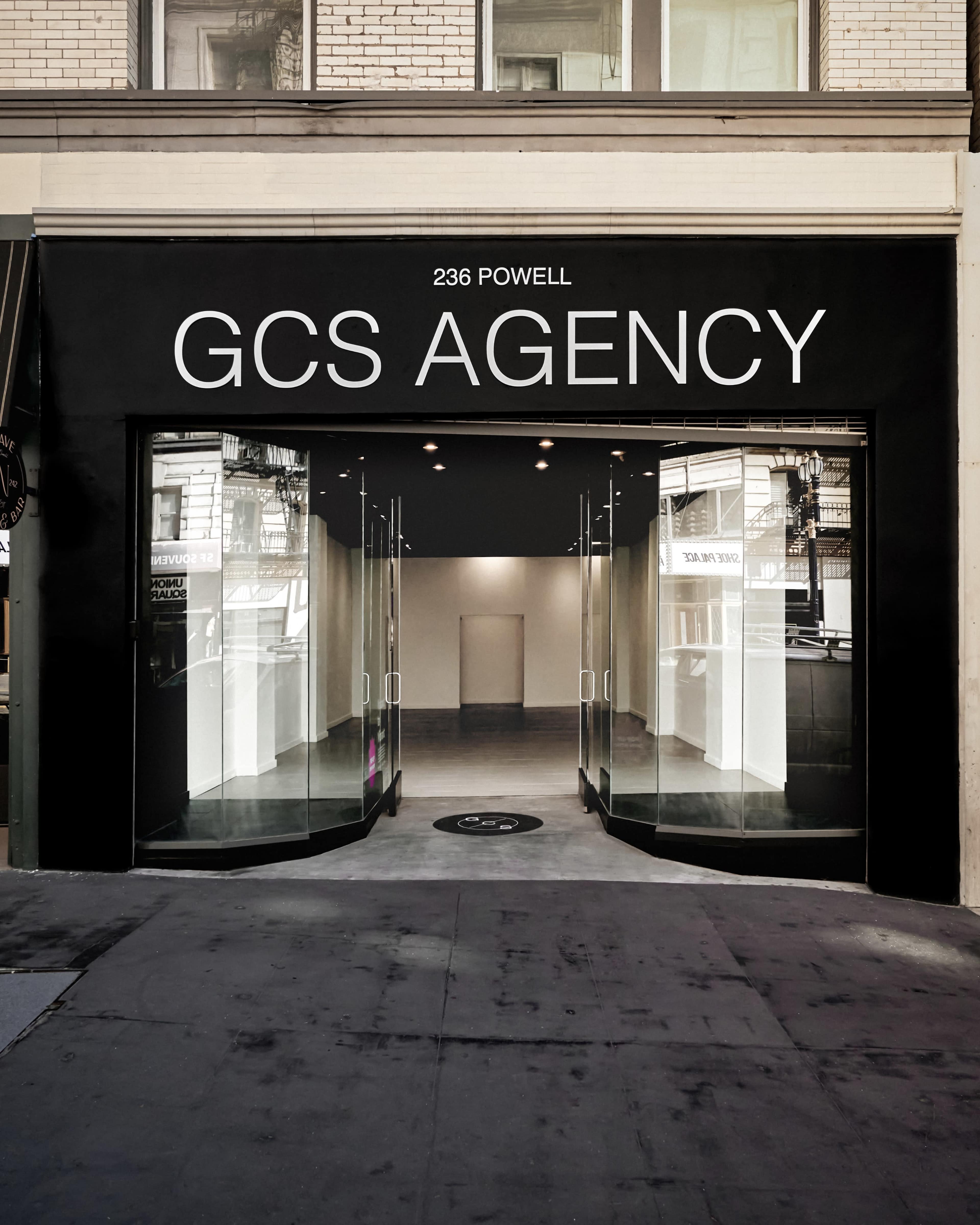 The image shows a modern storefront with large glass doors and a black facade displaying the text "GCS AGENCY" above the entrance at 236 Powell.