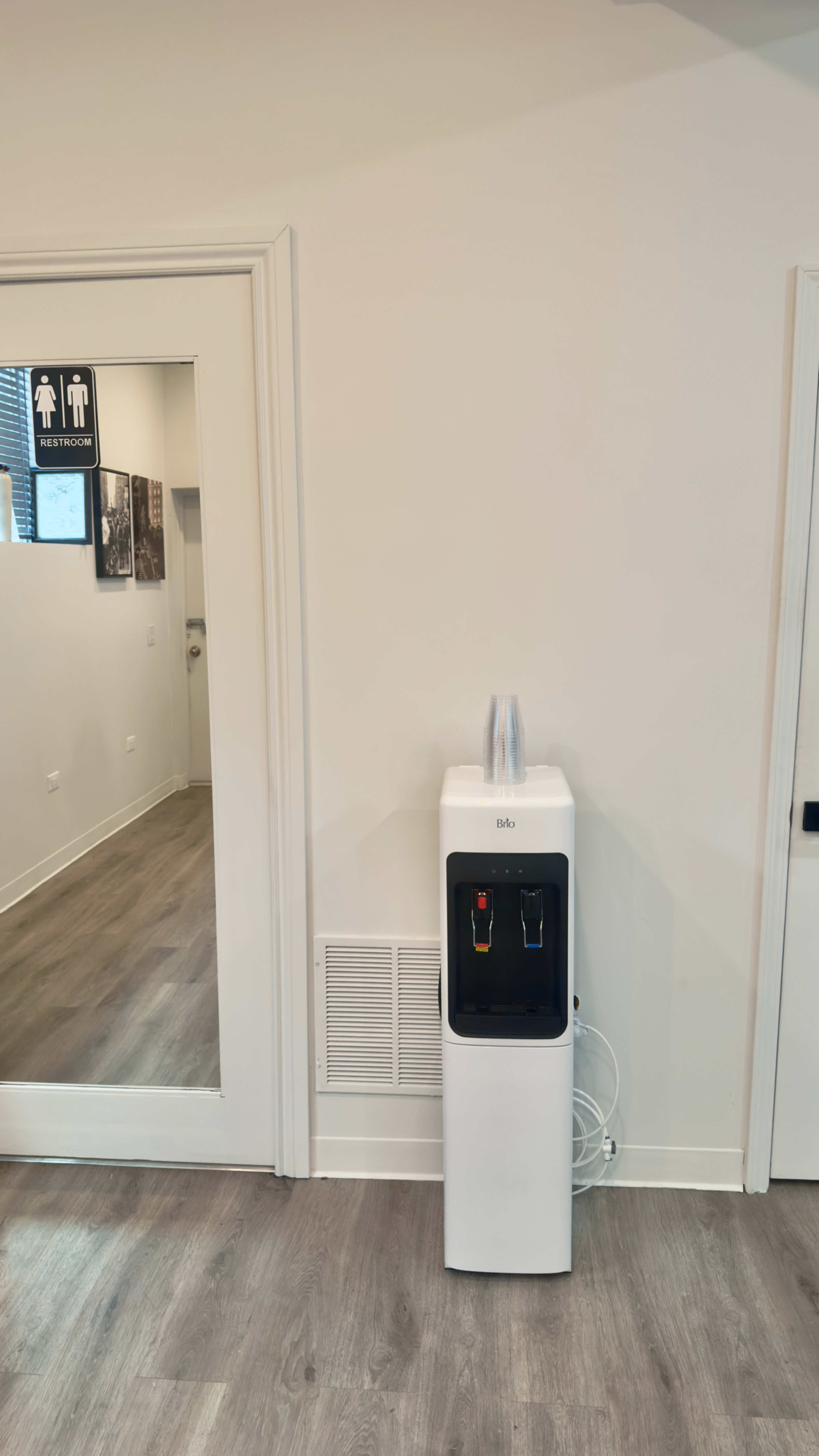 A white water cooler stands against a light-colored wall, next to a restroom entrance.