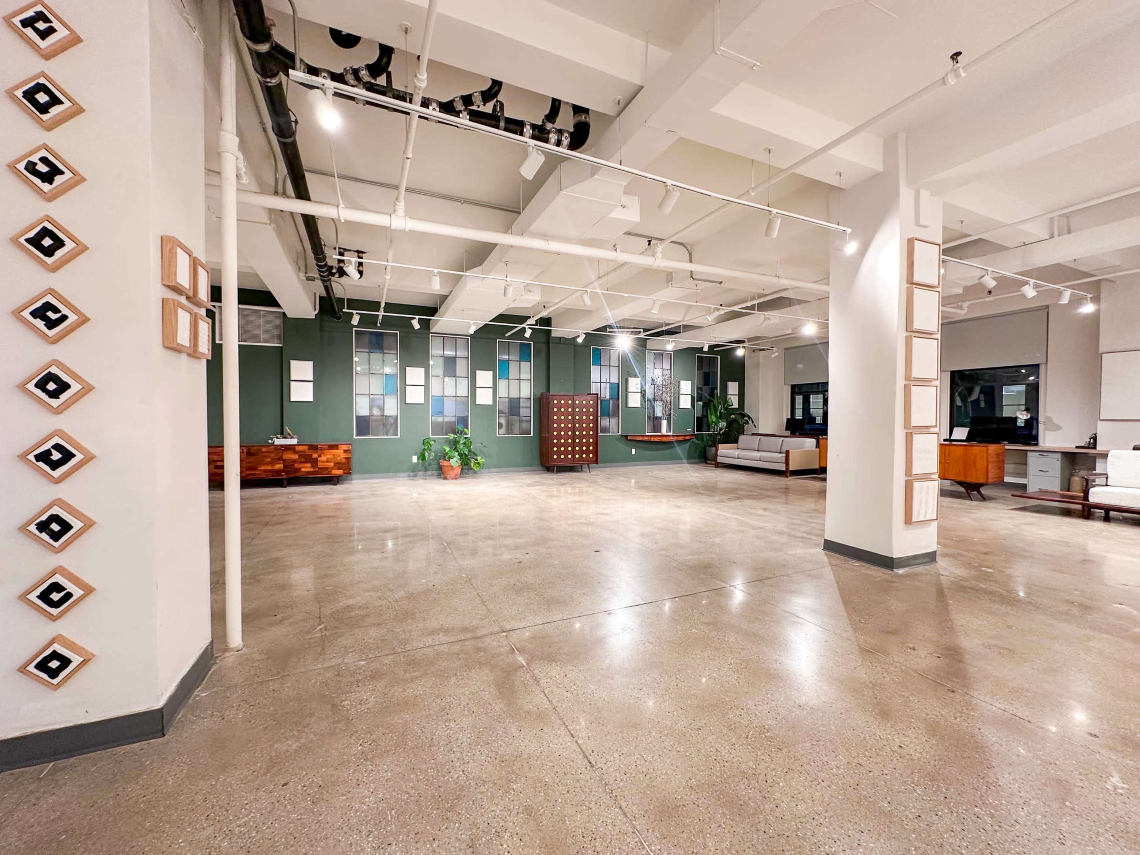 The image shows a spacious, modern interior with polished concrete floors, large windows, and minimalist furniture arranged in a bright, open layout.