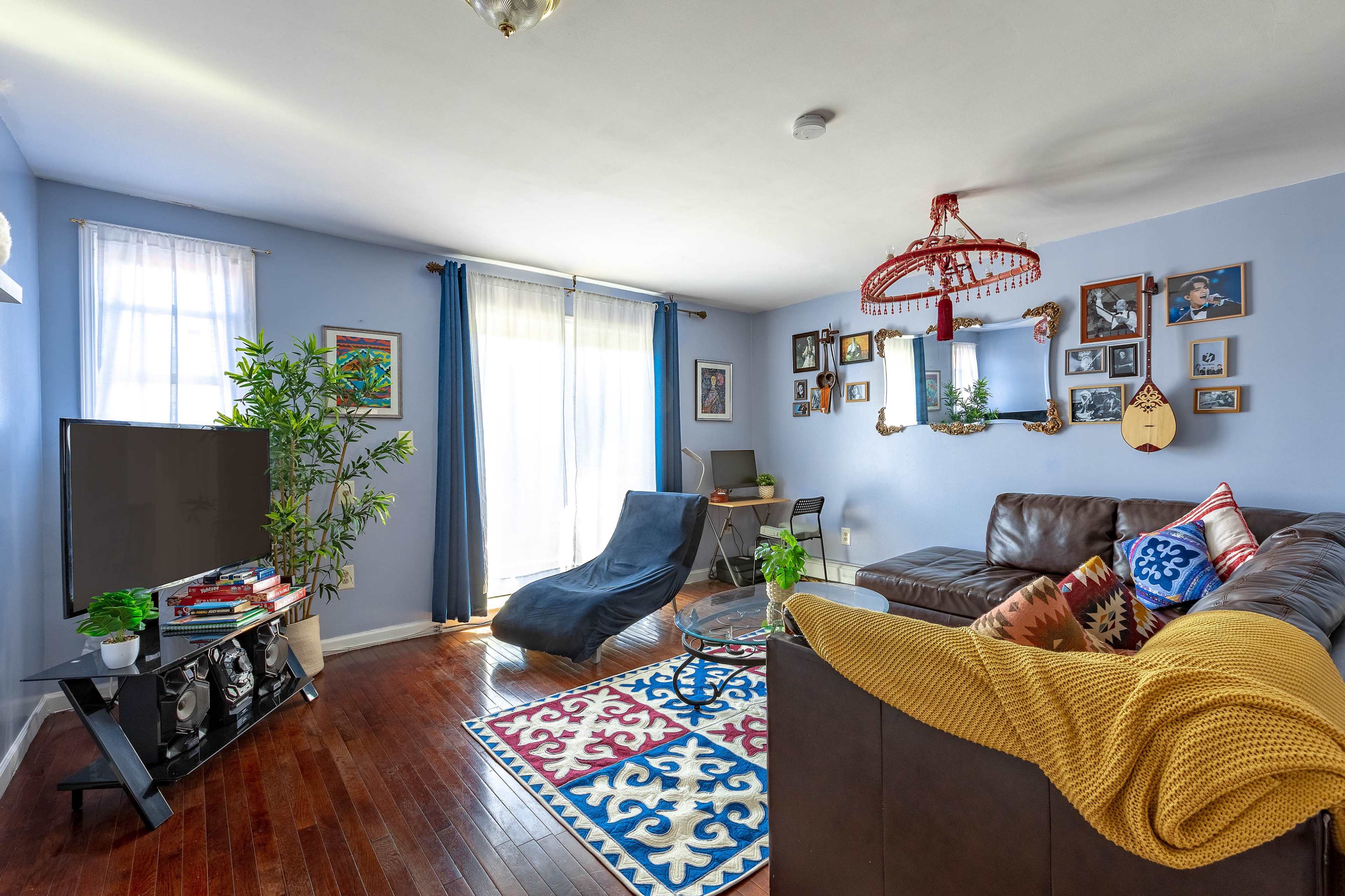 The living room features a brown sectional sofa, a large television, a colorful rug, and a wall adorned with various framed pictures.