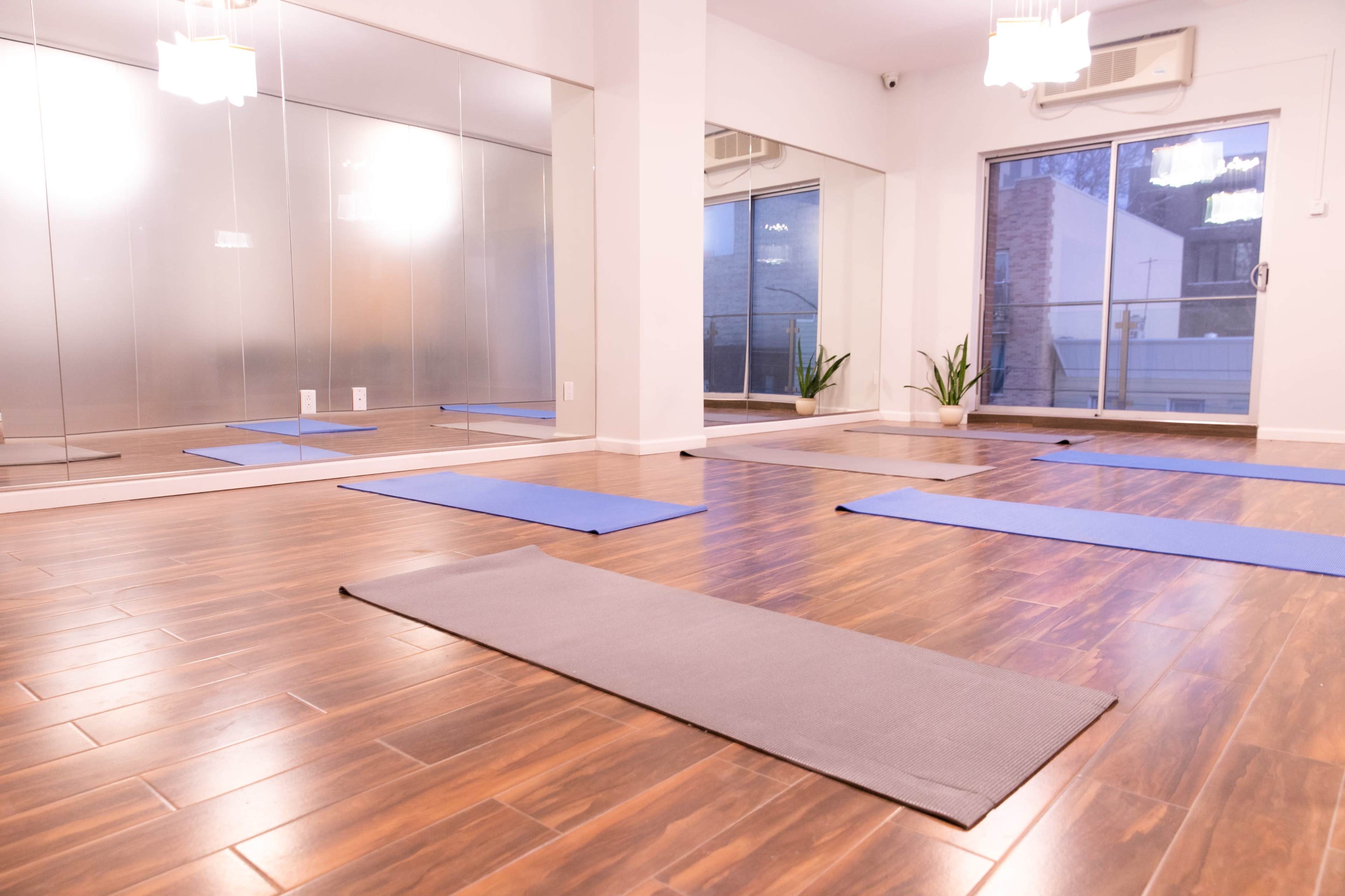 A yoga studio with several exercise mats laid out on a wooden floor and mirrors lining one wall.