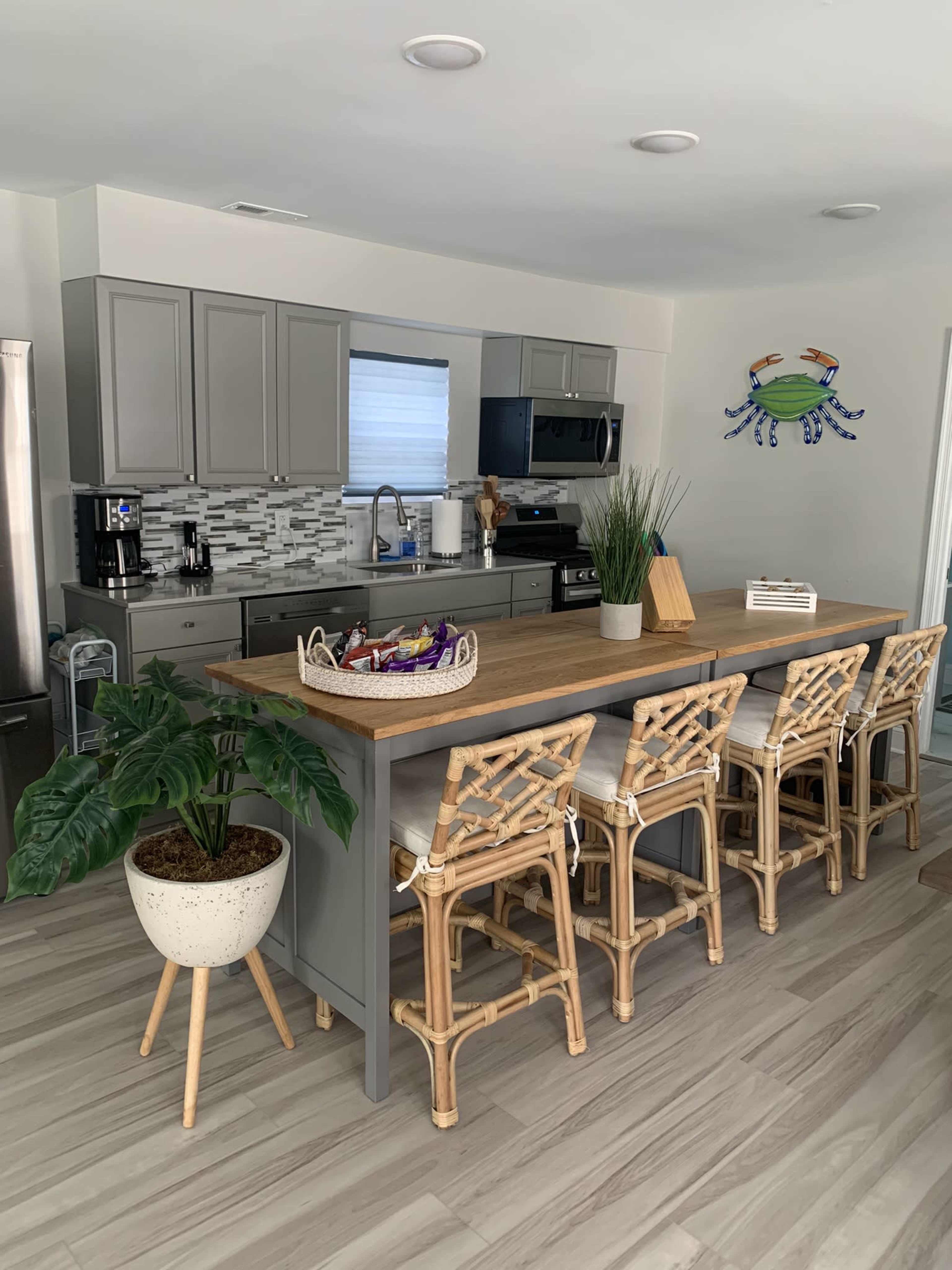 A modern kitchen features gray cabinets, stainless steel appliances, a wooden island with seating, and a decorative crab wall art.
