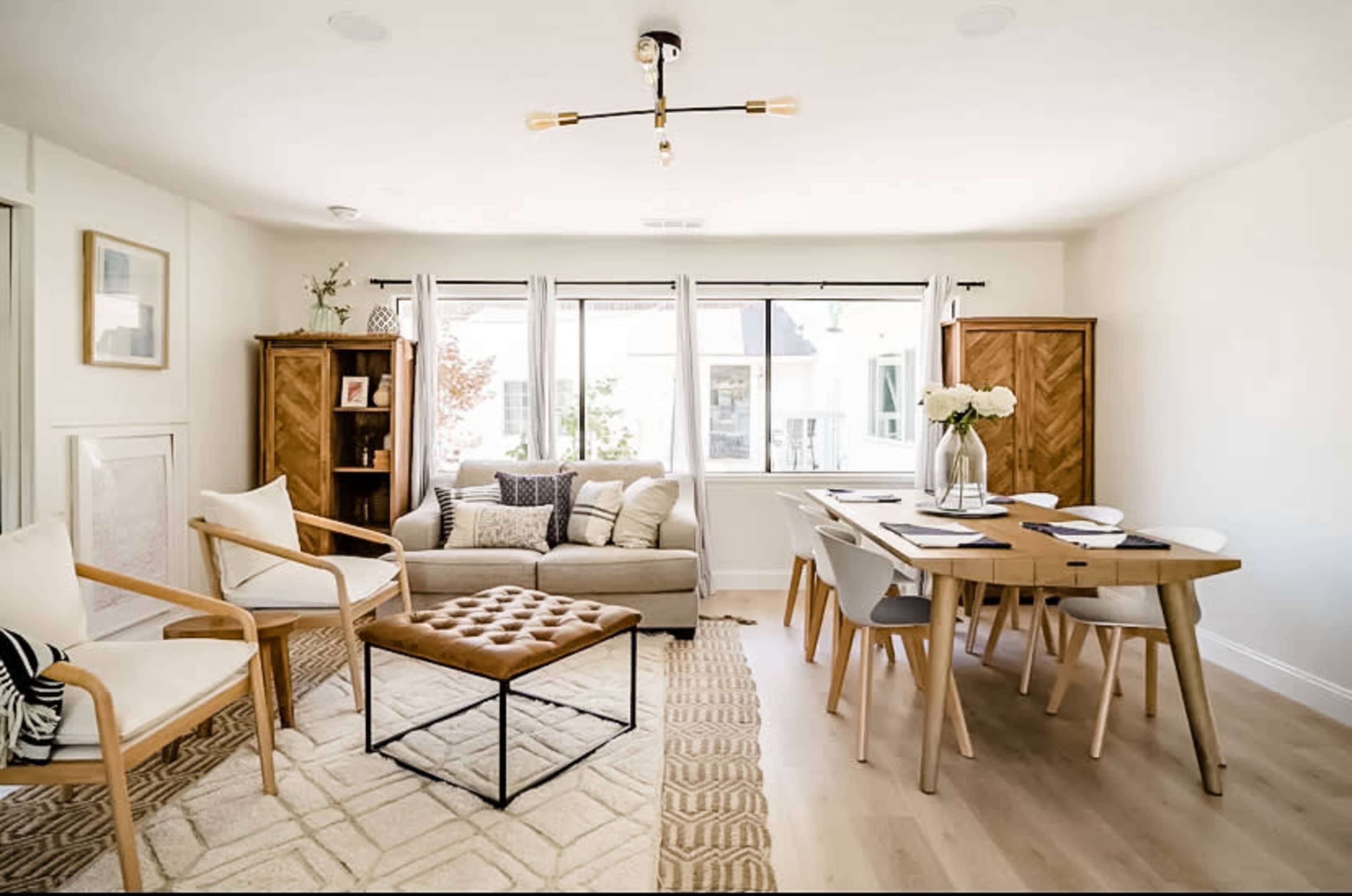 A bright living and dining area featuring a sofa, armchairs, a coffee table, and a dining table with chairs.