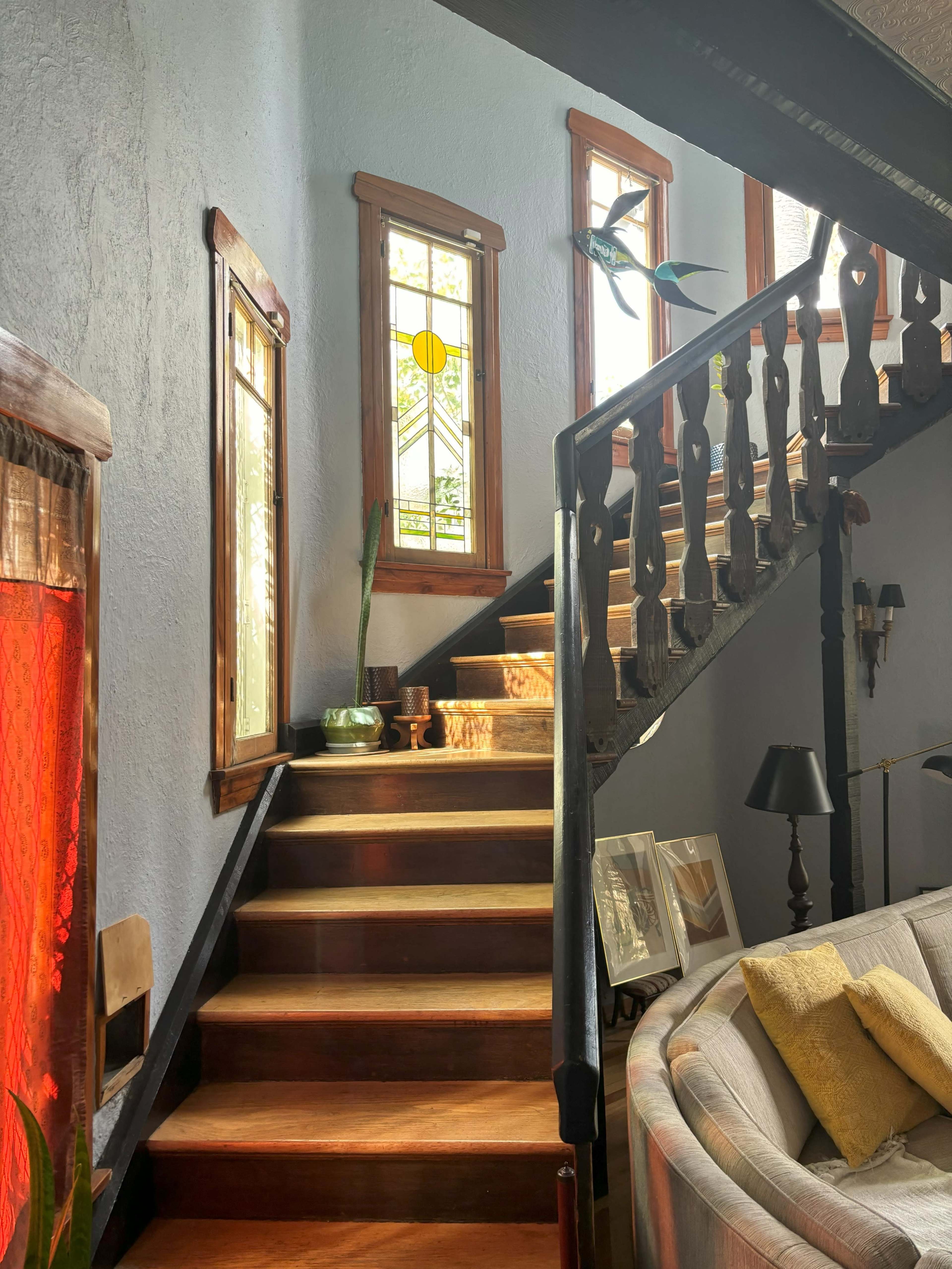 A staircase with wooden steps leading up to a landing, flanked by stained glass windows and a cozy seating area to the right.