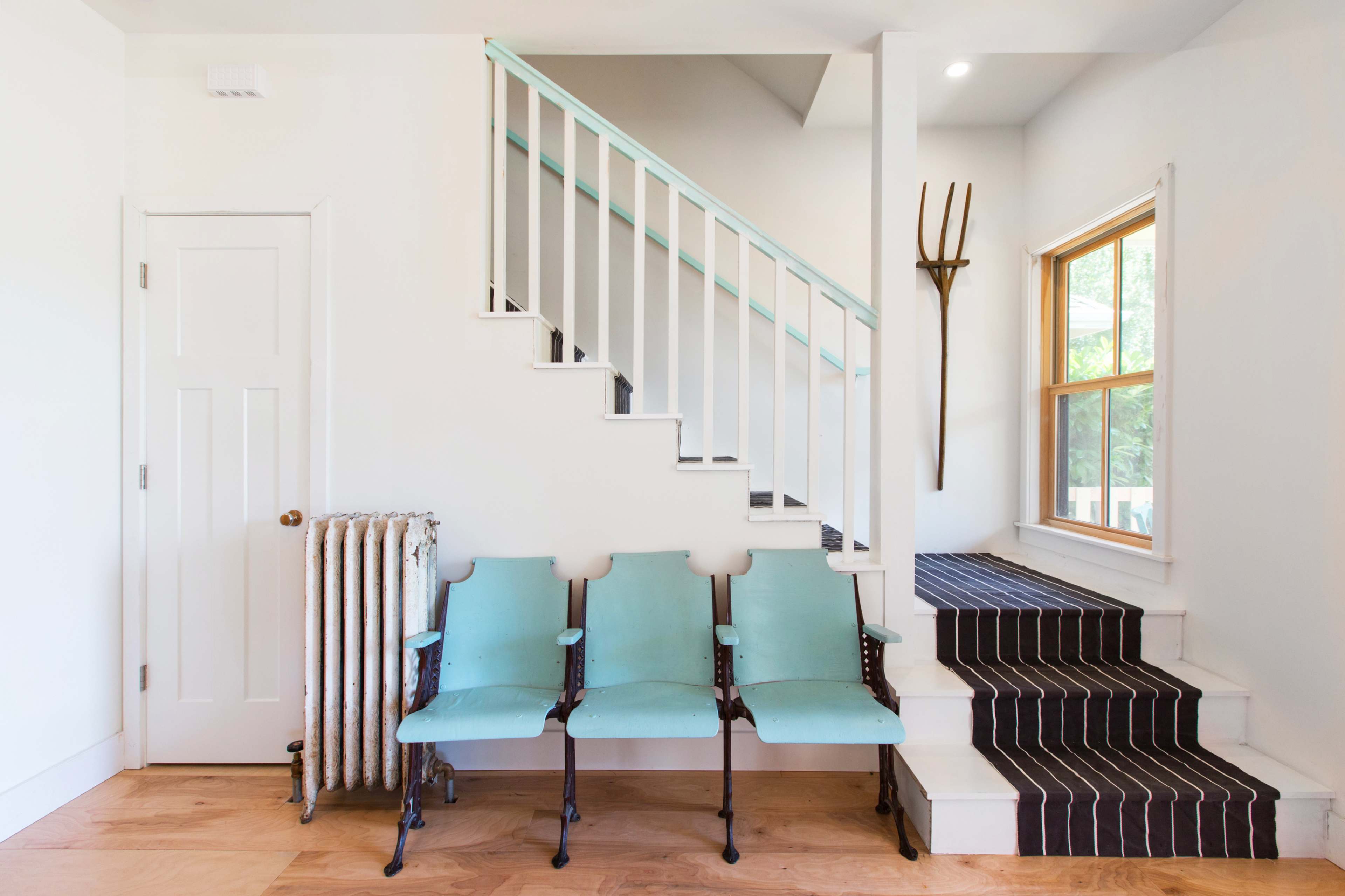 A minimalist entryway with three blue chairs, a staircase leading to an upper level, and a wooden floor with a striped rug.