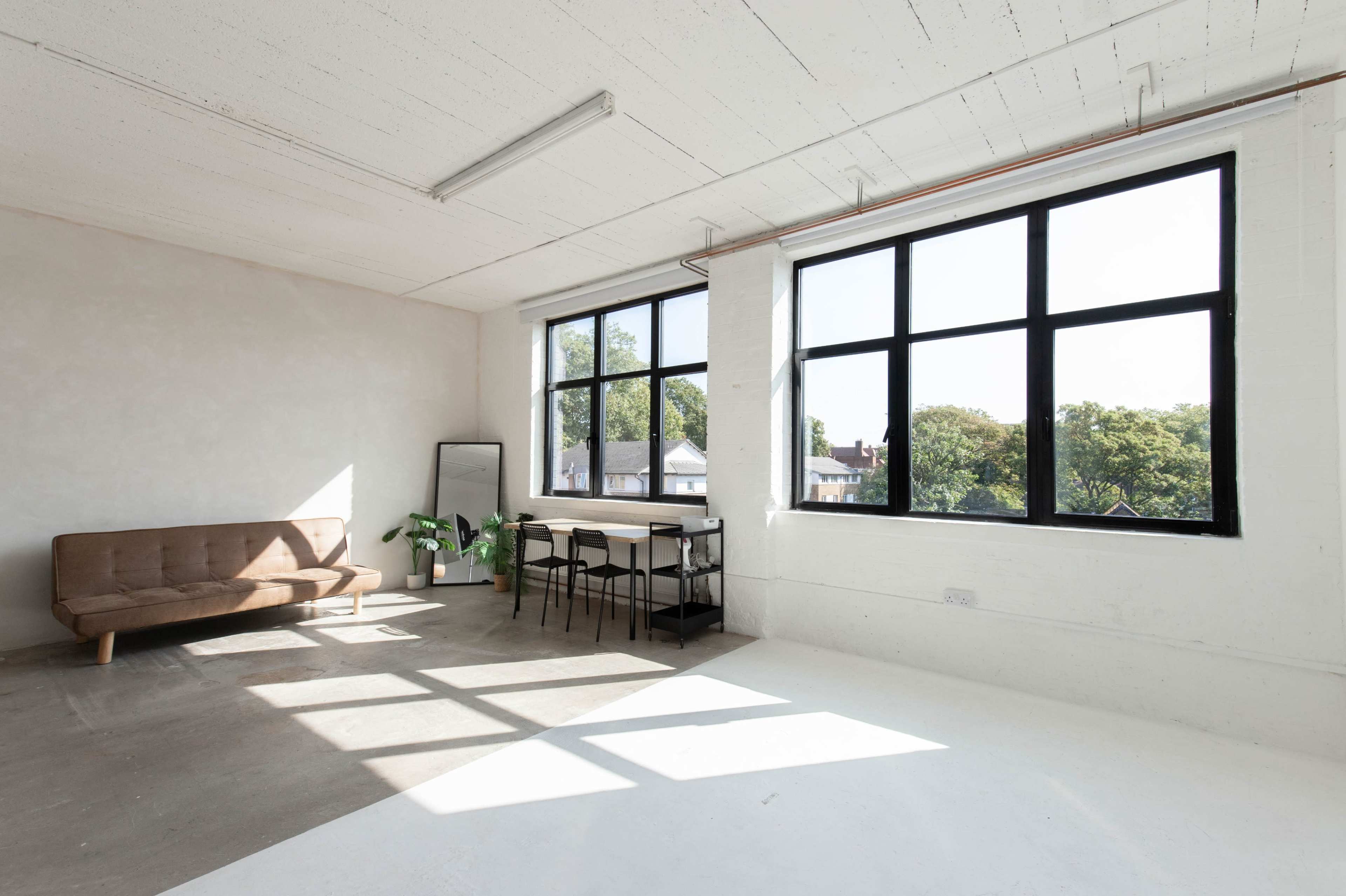 A spacious, well-lit room with large windows, a brown sofa, a dining table with chairs, and a mirror.