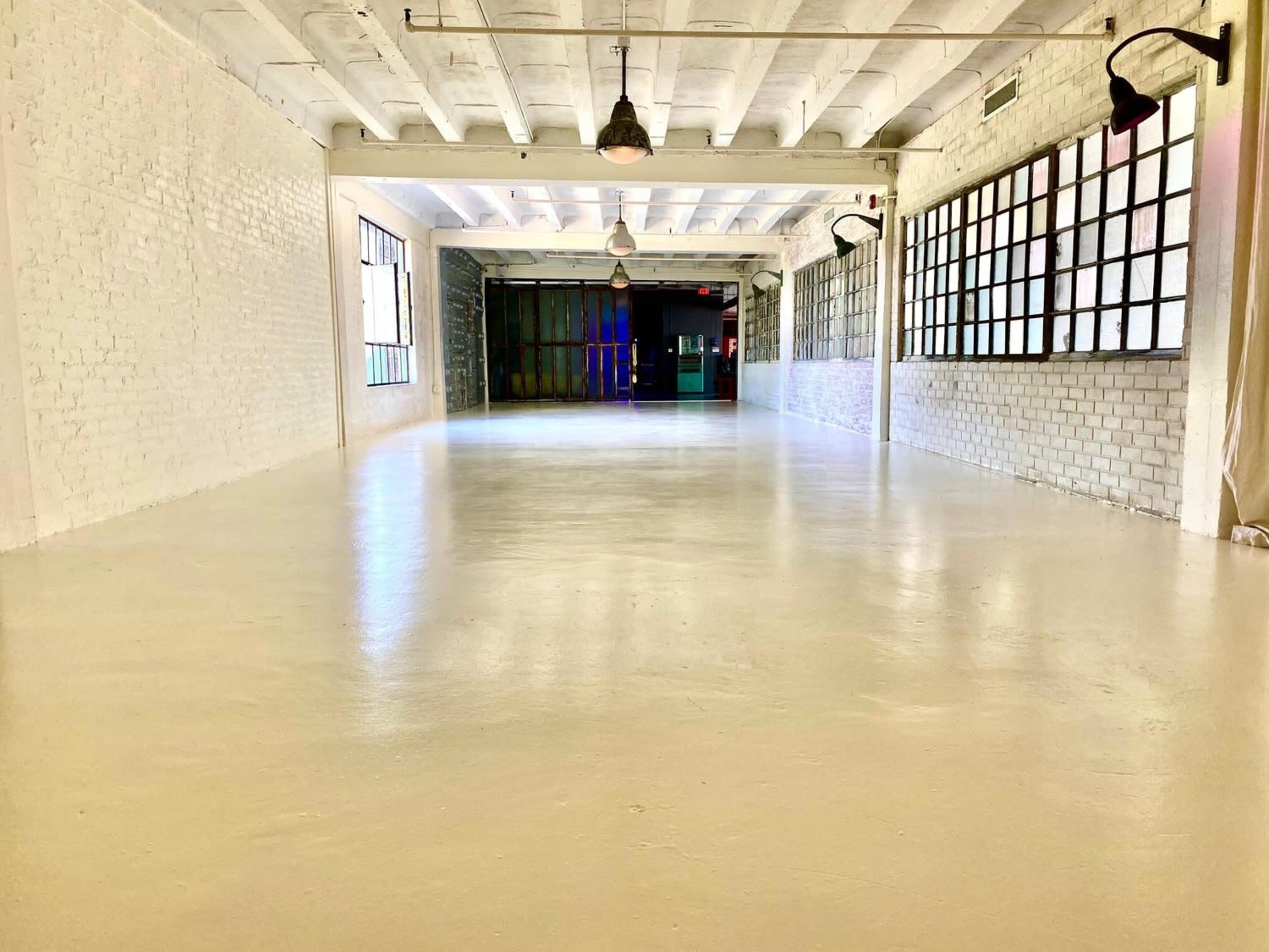 A spacious, brightly lit warehouse interior with white walls and large windows along one side.
