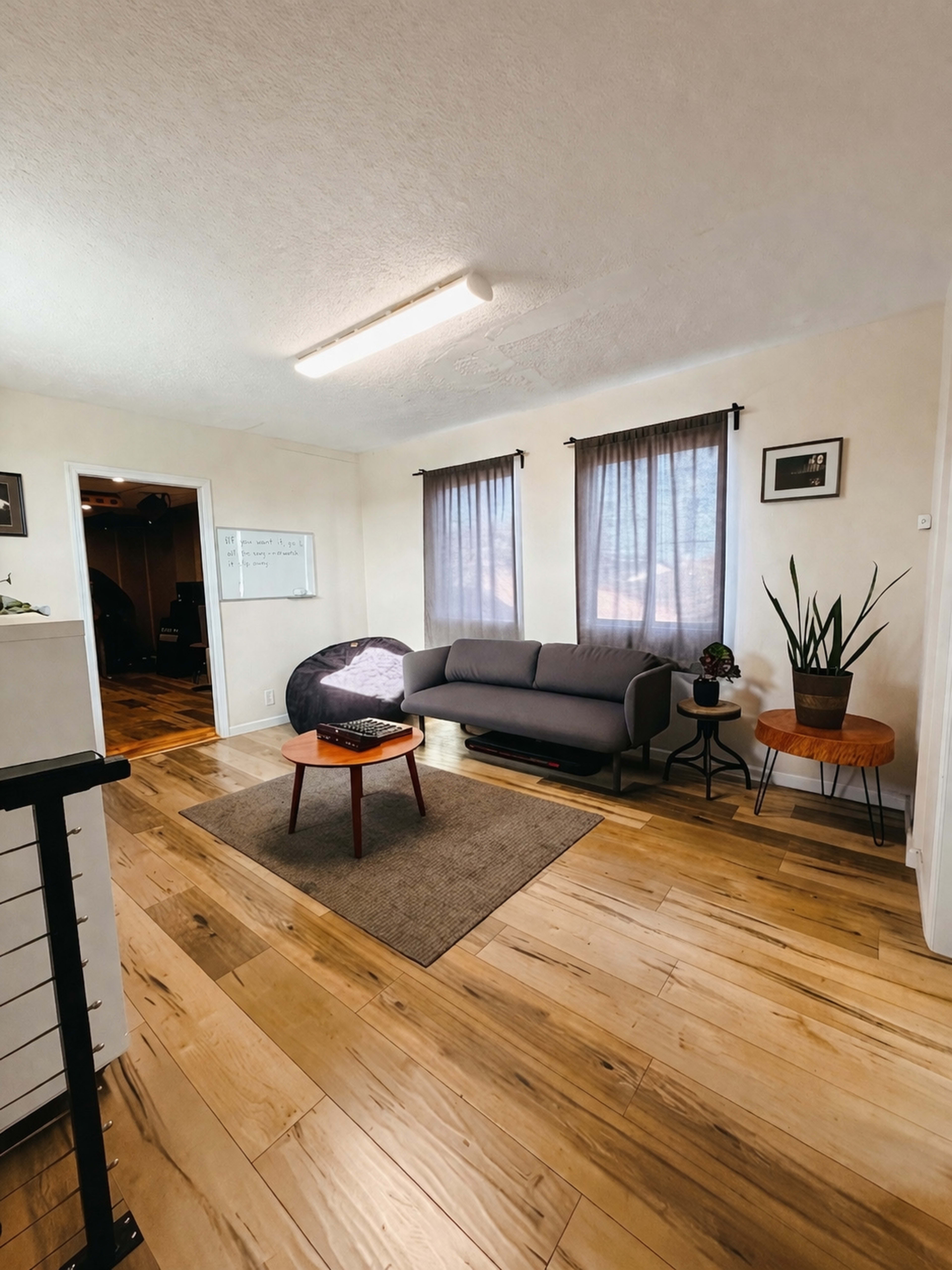 The image shows a living room with a gray couch, a small wooden table, a carpet, and curtains framing a window.