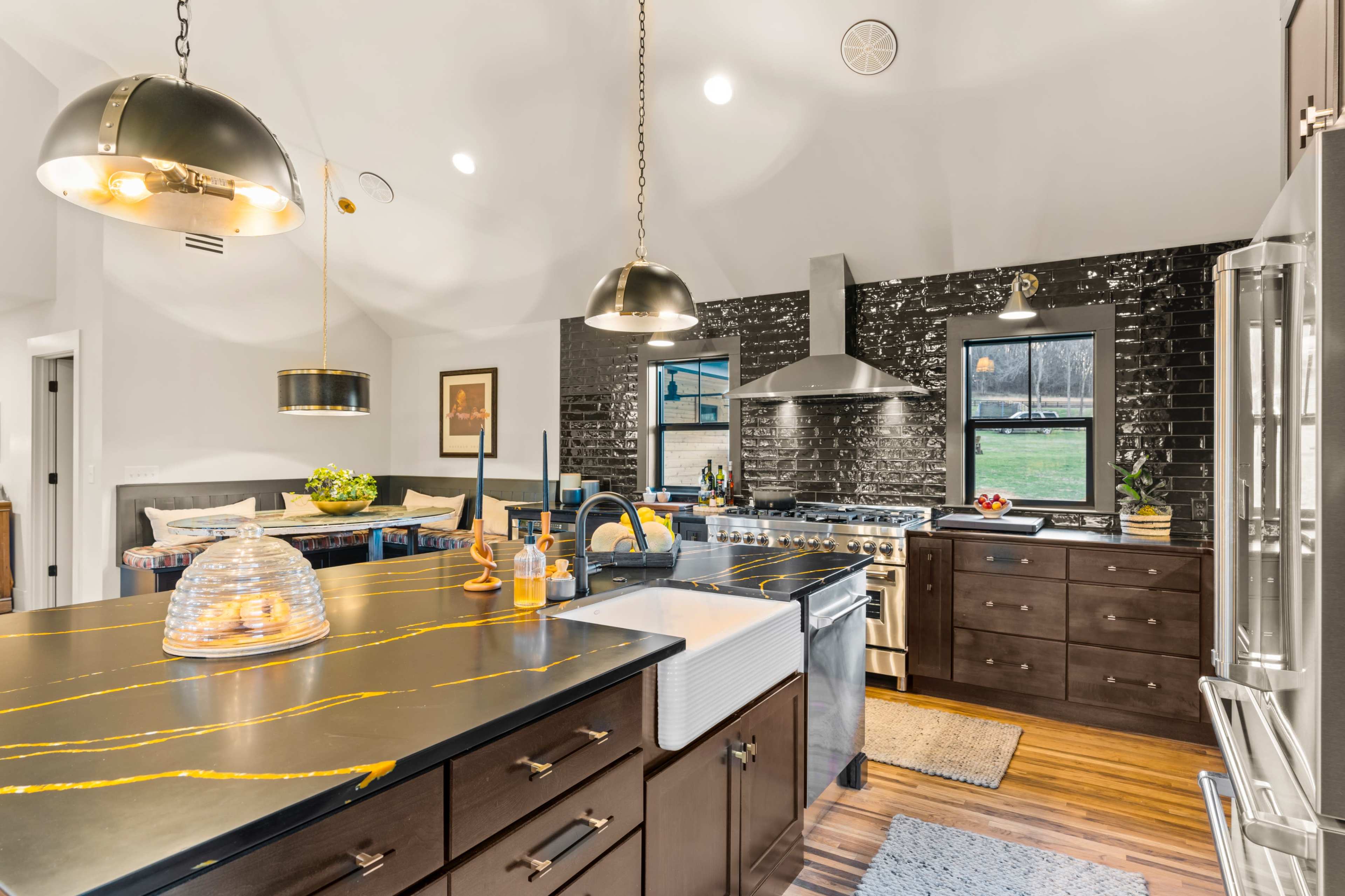 The kitchen features a large island with a black countertop and gold veining, stainless steel appliances, and a mix of pendant lighting above.