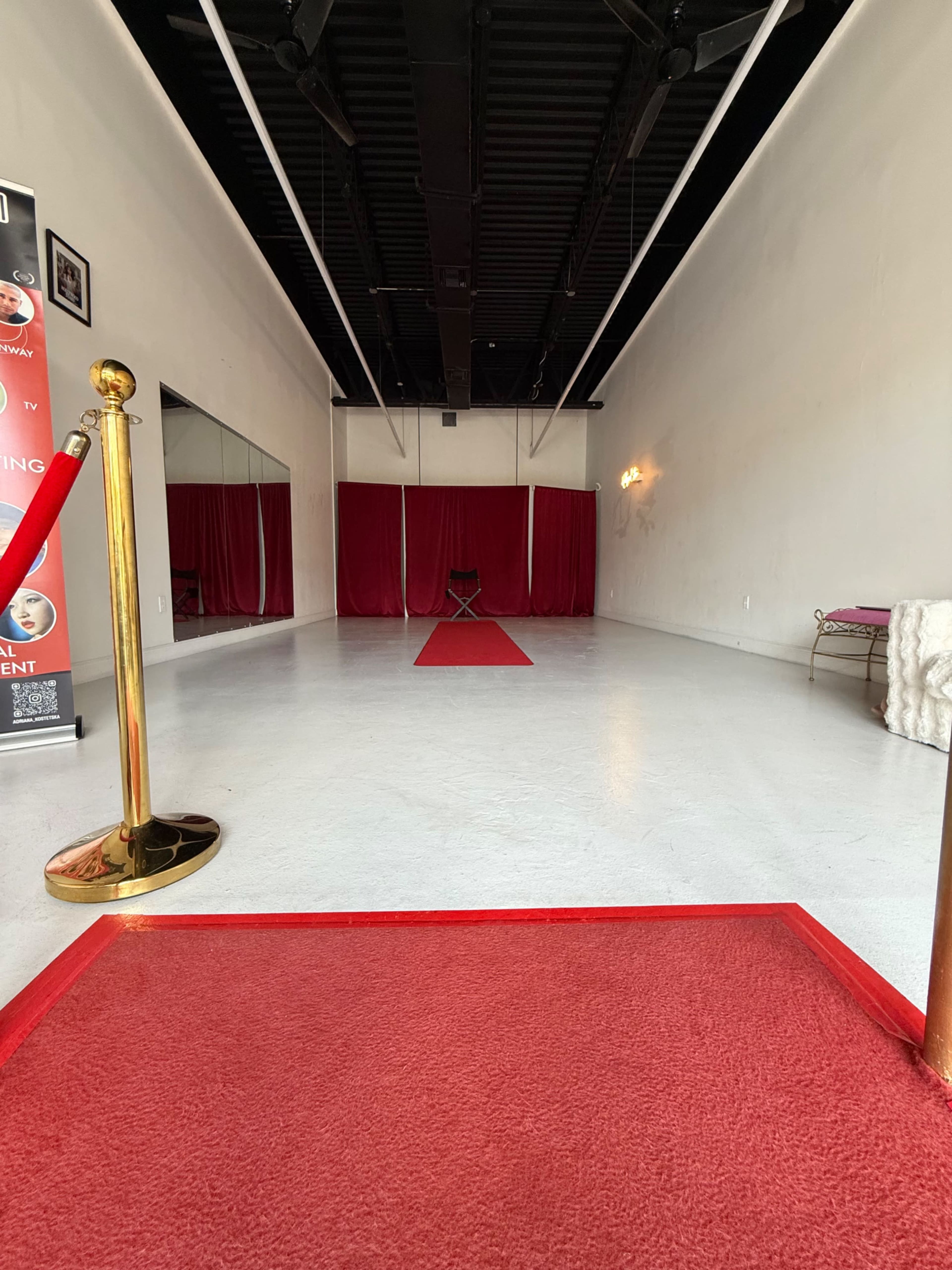 The image shows a spacious, vacant room featuring a red carpet leading to a chair, flanked by red curtains and a small mirrored wall.