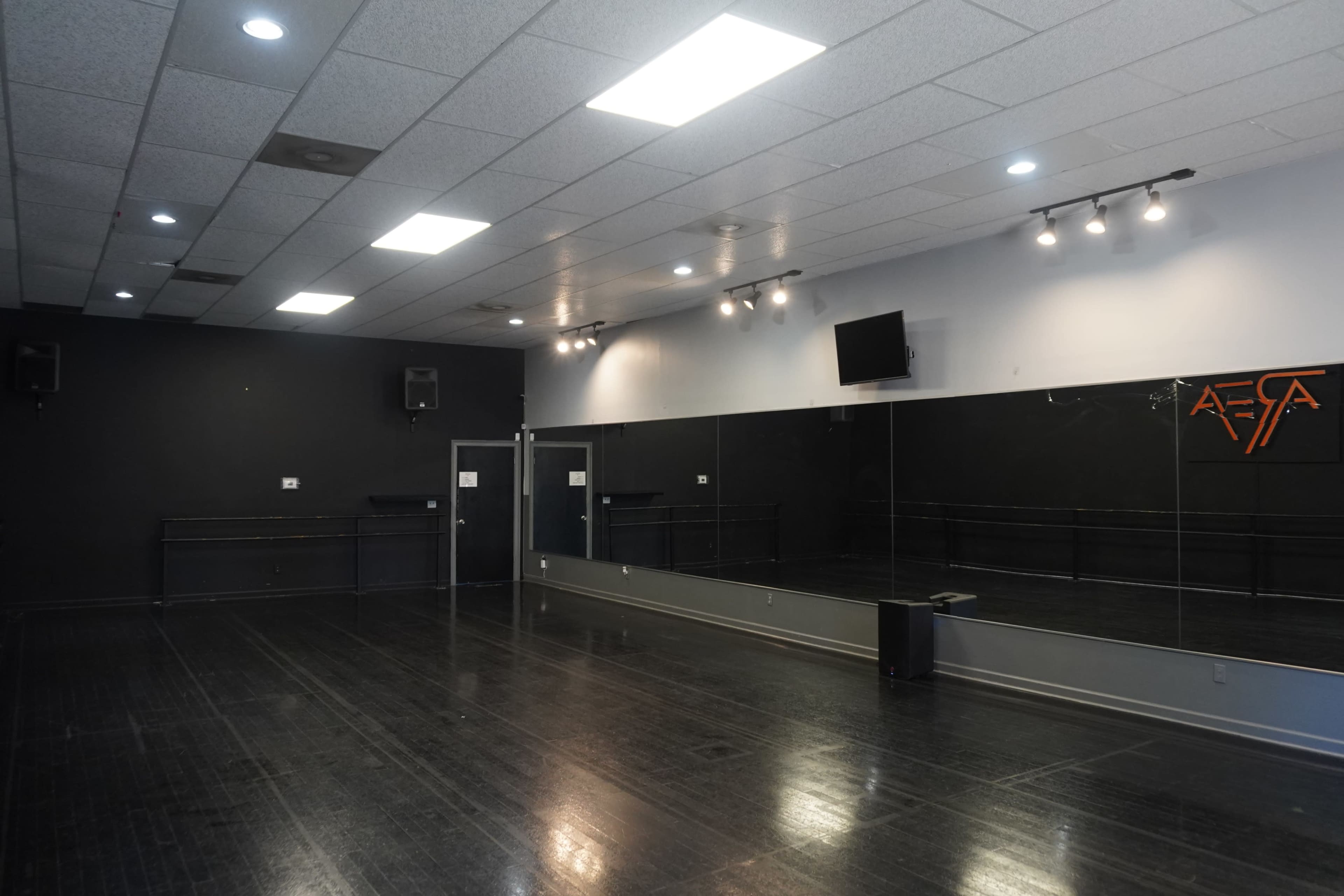 An empty dance studio with a wooden floor, mirrored wall, and overhead lights.