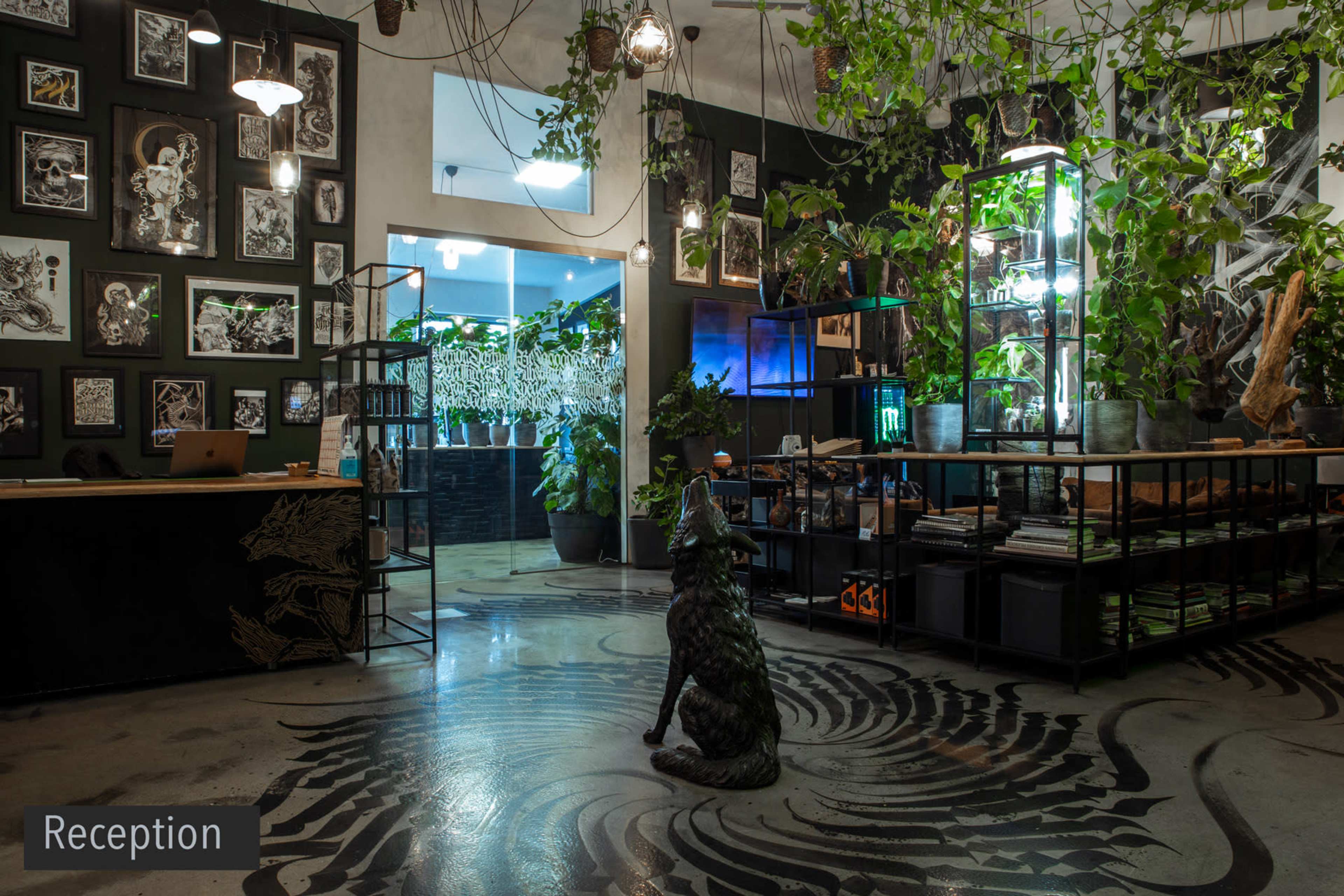 A reception area featuring a black wall adorned with framed artwork, shelves filled with plants and books, and a decorative sculpture of a dog on the floor.