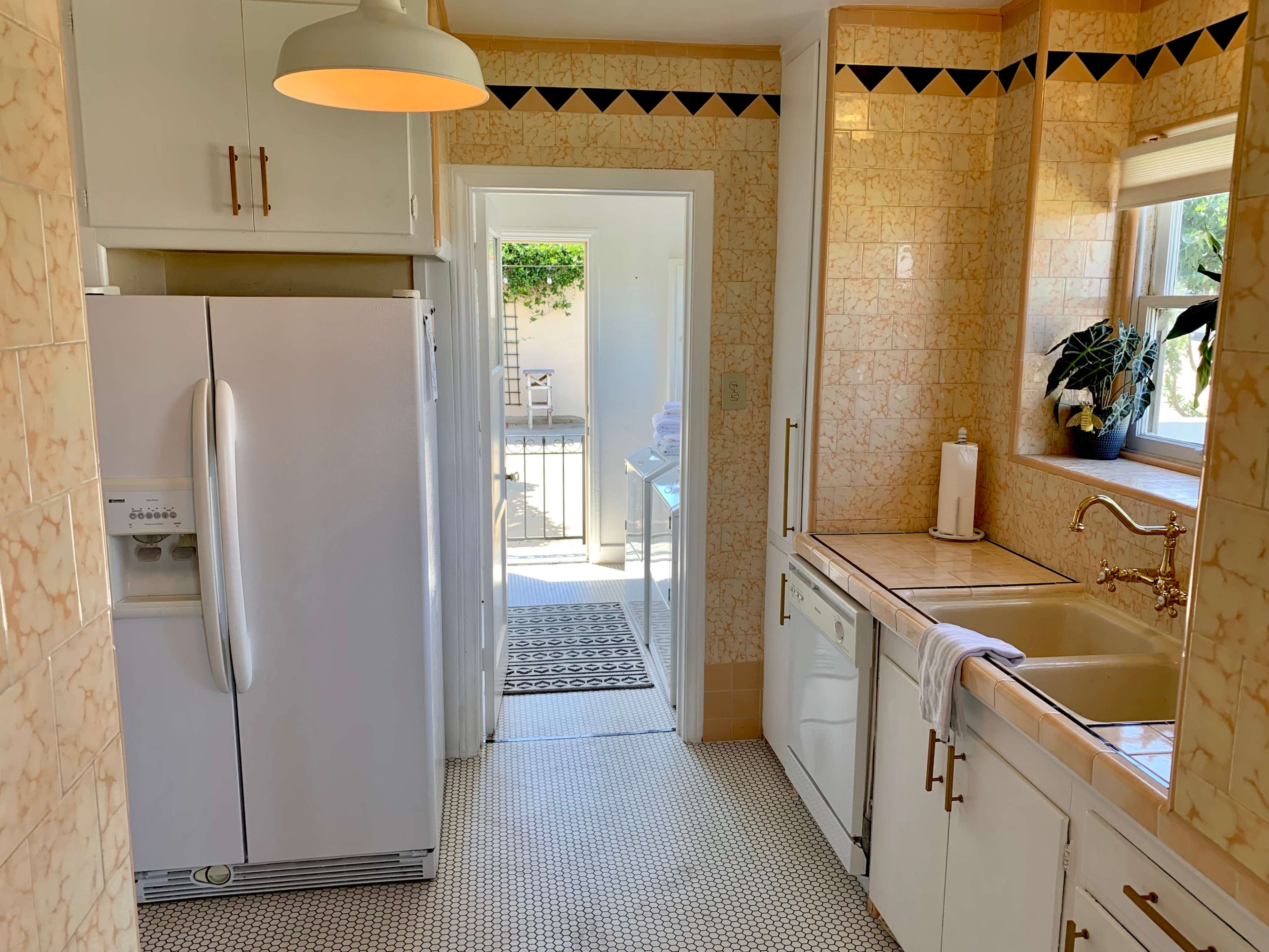 A clean kitchen features a white refrigerator, sink, and dishwasher, with a door leading to an outdoor space.