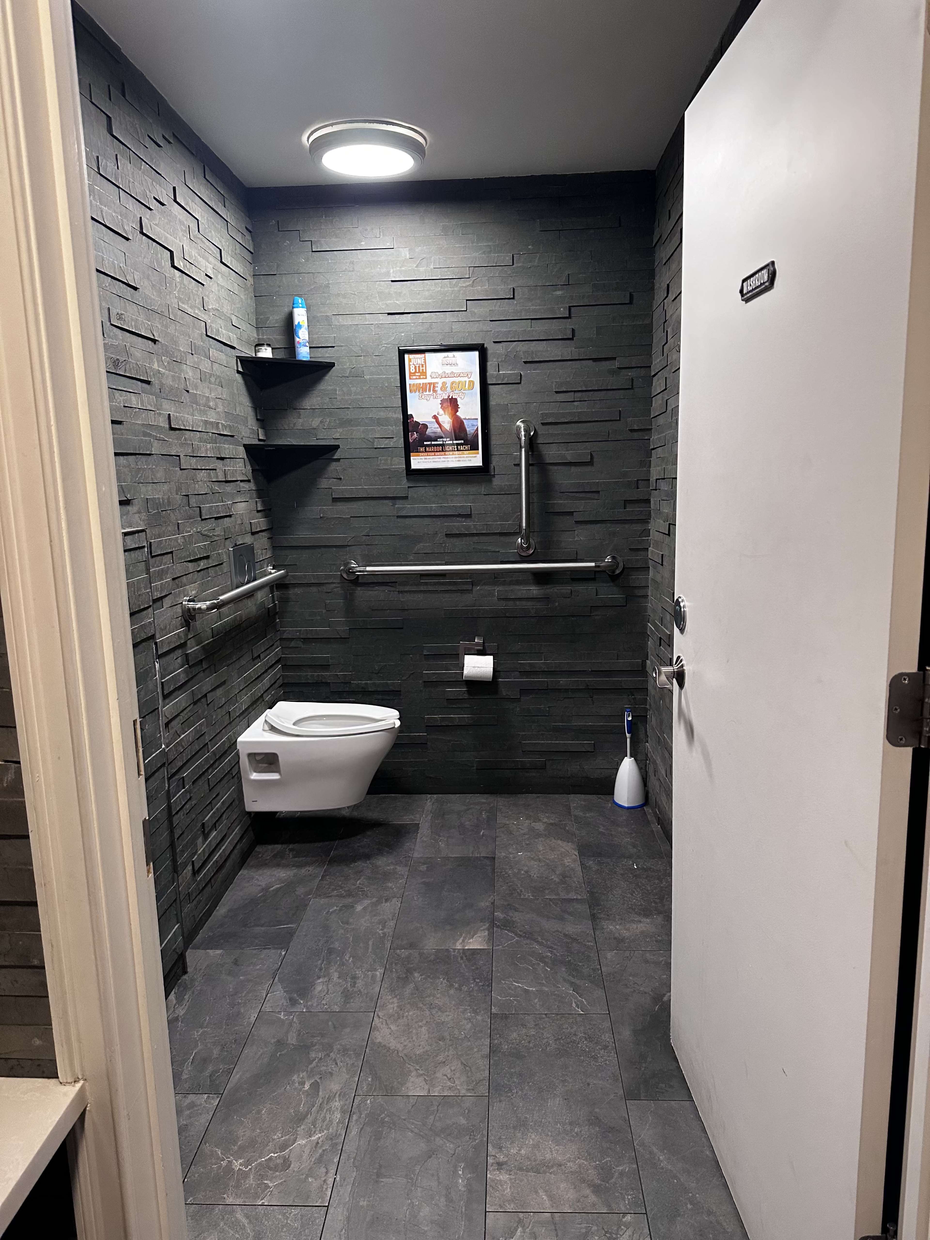 The image shows a modern restroom with stone-like walls, featuring a toilet, shelves, and a door labeled "Men."