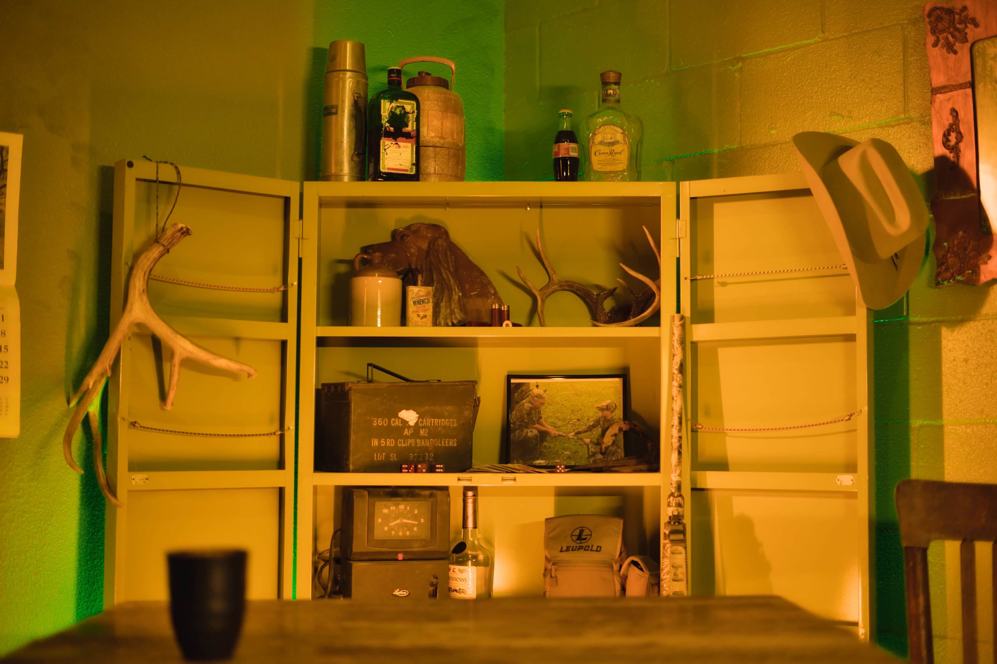 A shelf filled with various bottles, containers, and antlers against a green-lit wall.