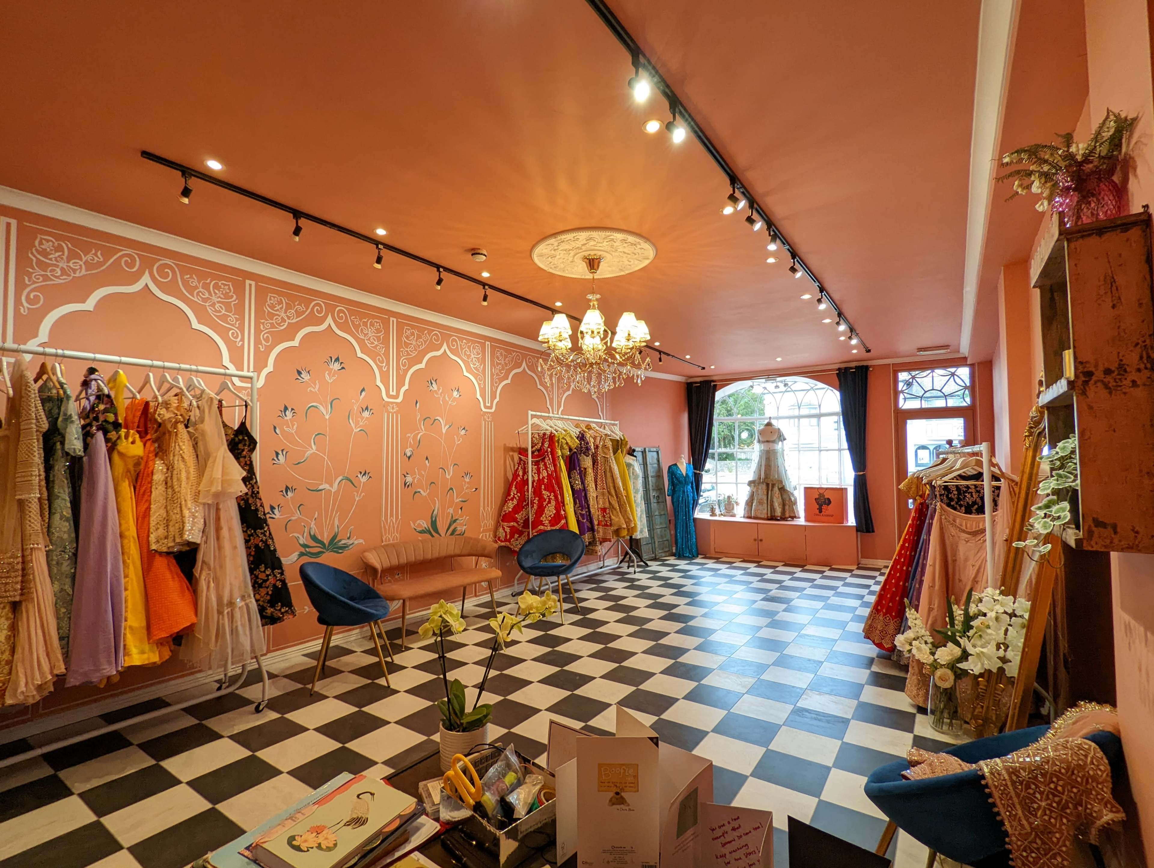 A boutique displays a variety of colorful dresses against a peach-colored wall, with a checkered floor and a chandelier above.