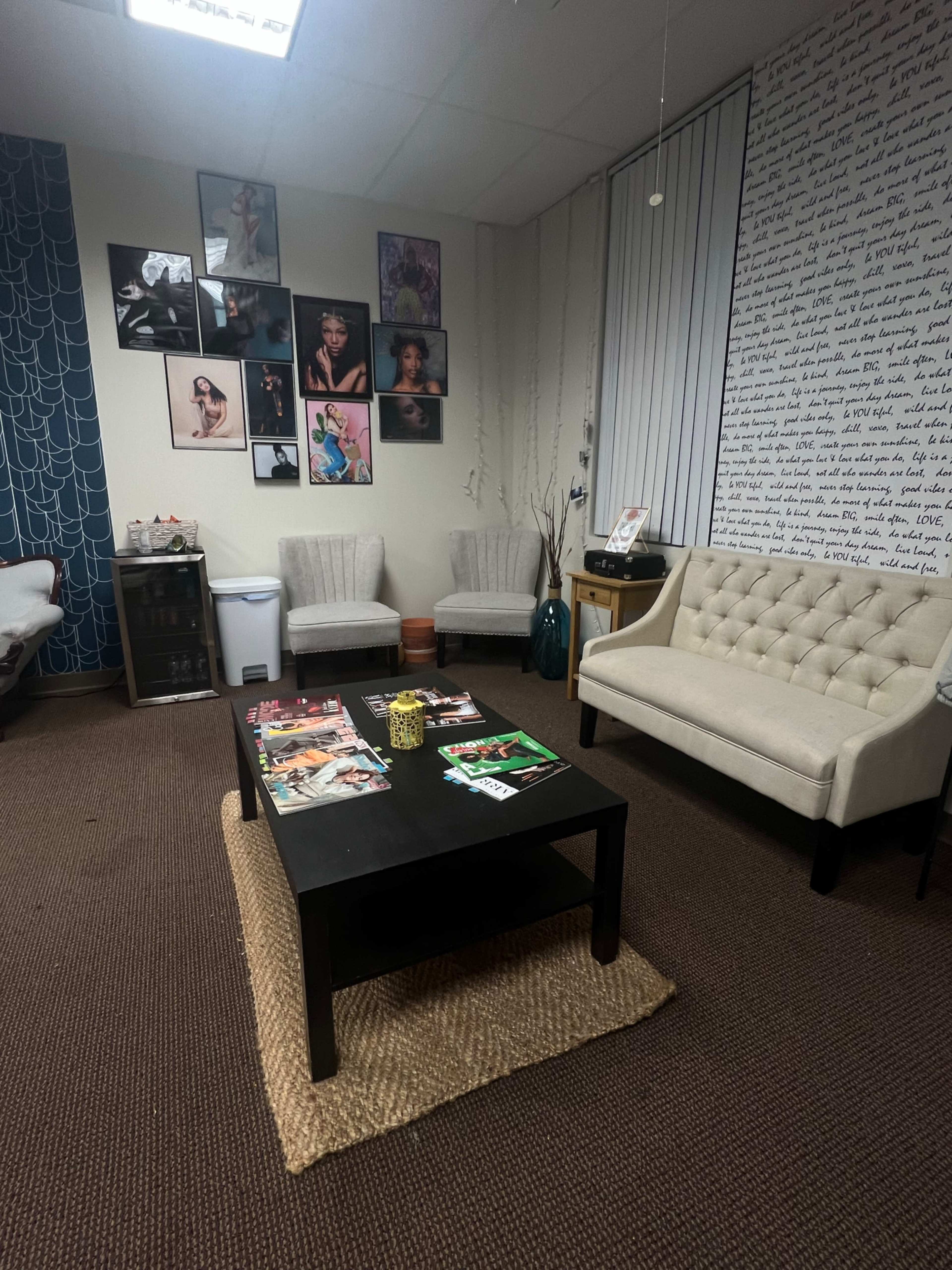 The room features a seating area with a light-colored couch and chairs, a black coffee table adorned with magazines, and walls decorated with framed photographs and a handwritten text mural.