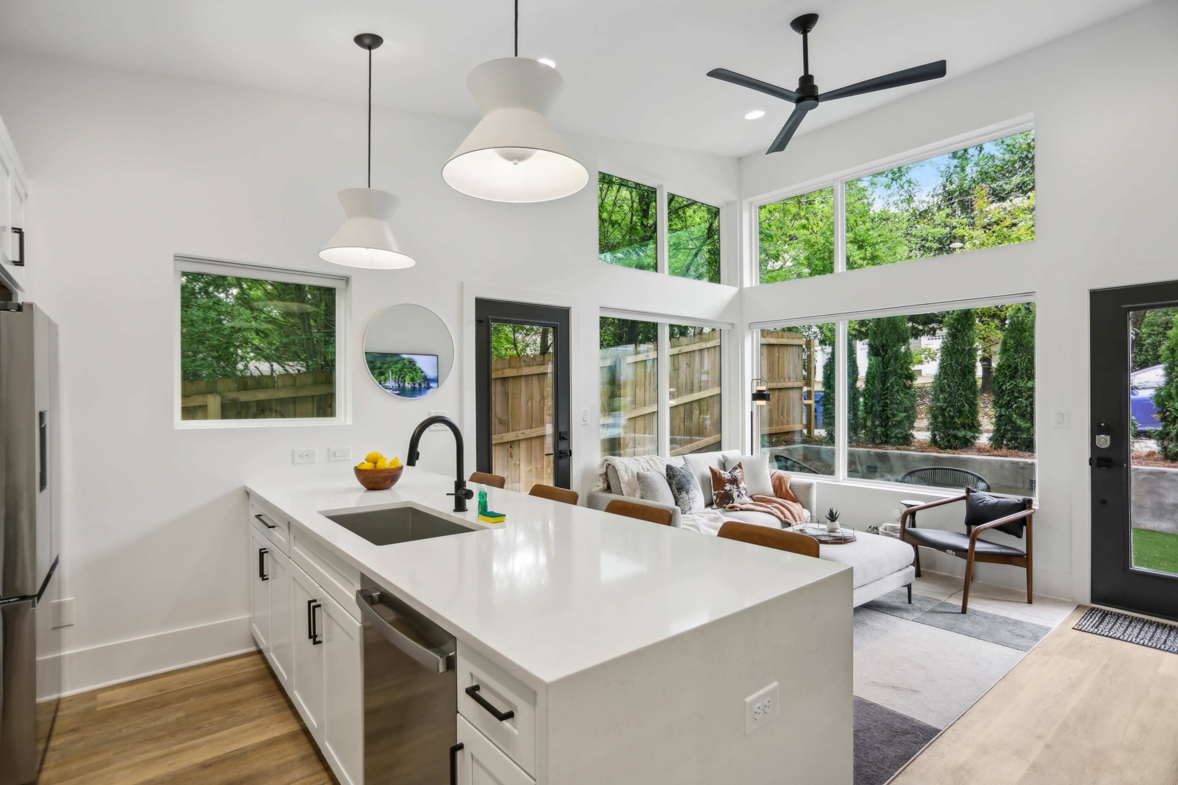 A modern kitchen with white cabinetry, a large island, and large windows allowing natural light to fill the space, complemented by a cozy seating area nearby.